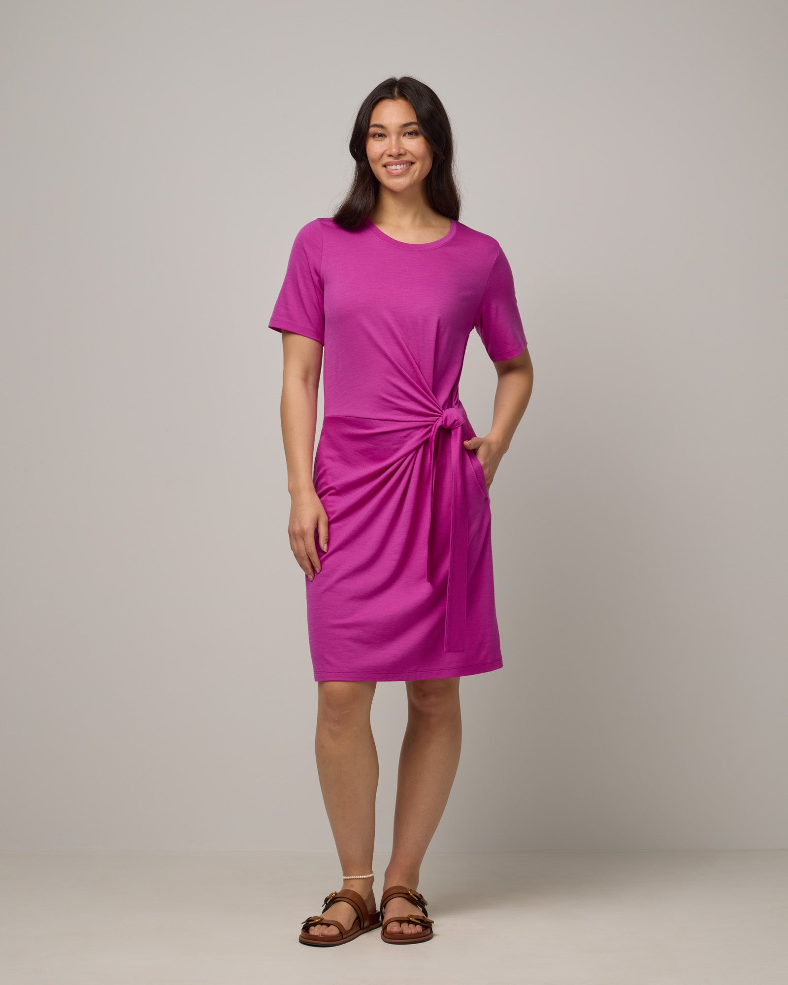 Model wearing Kelly Faux Tie Dress in Petunia, a bright fuchsia pink color. Kelly Faux Tie Dress is a merino wool crew neck, short sleeve, knee length shift dress with pockets available in sizes XS-3X. 