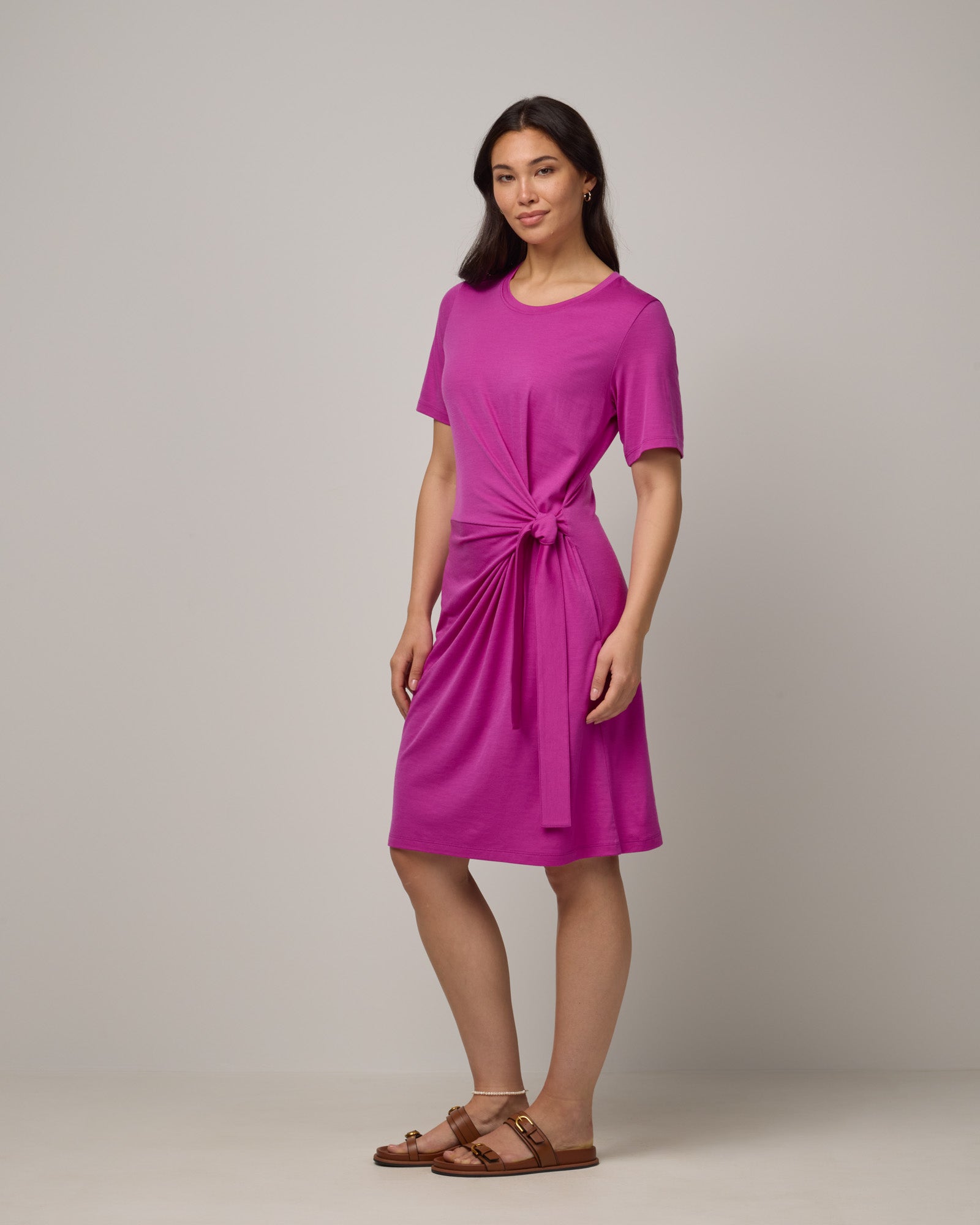 Model wearing Kelly Faux Tie Dress in Petunia, a bright fuchsia pink color. Kelly Faux Tie Dress is a merino wool crew neck, short sleeve, knee length shift dress with pockets available in sizes XS-3X. 