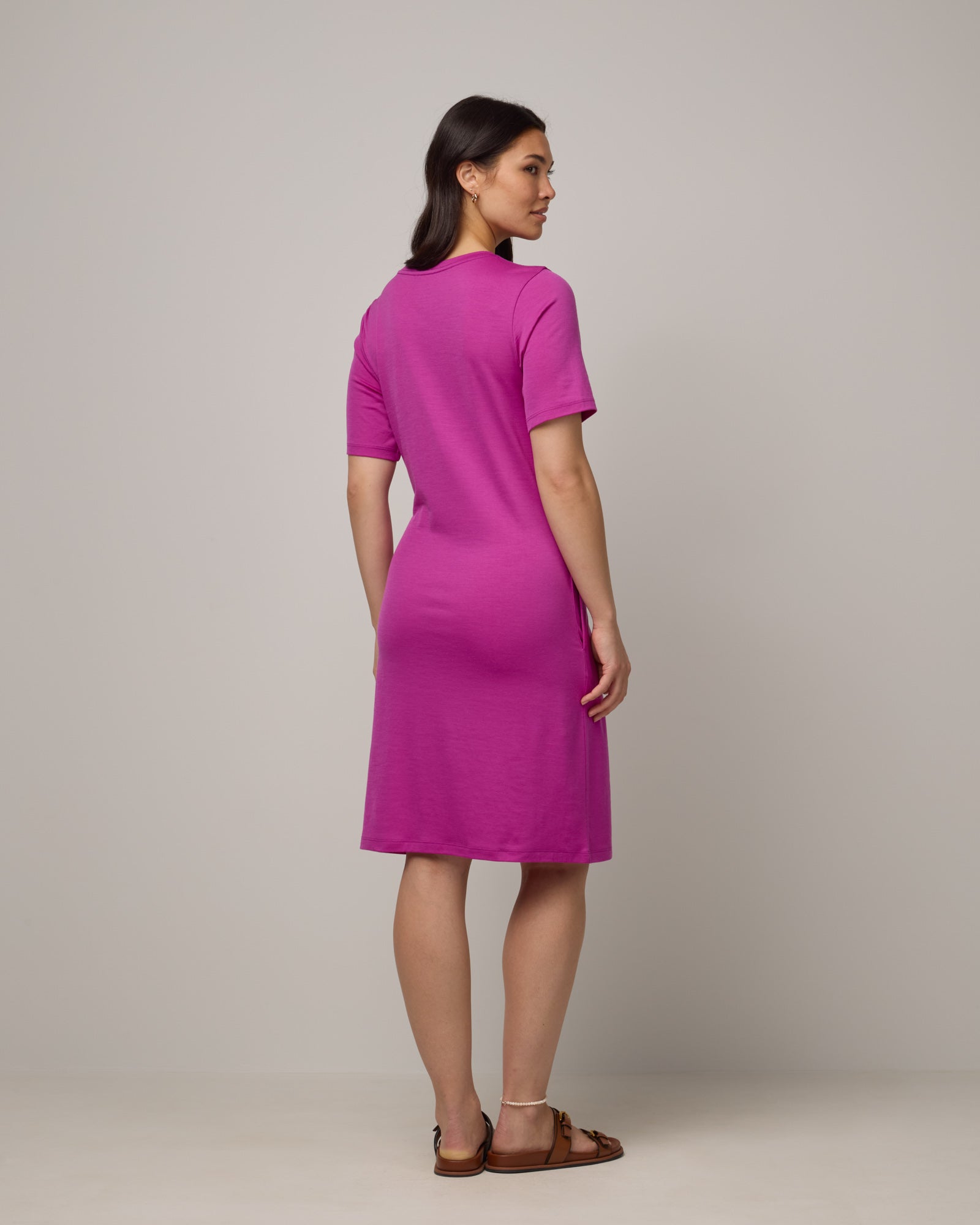 Model wearing Kelly Faux Tie Dress in Petunia, a bright fuchsia pink color. Kelly Faux Tie Dress is a merino wool crew neck, short sleeve, knee length shift dress with pockets available in sizes XS-3X. 