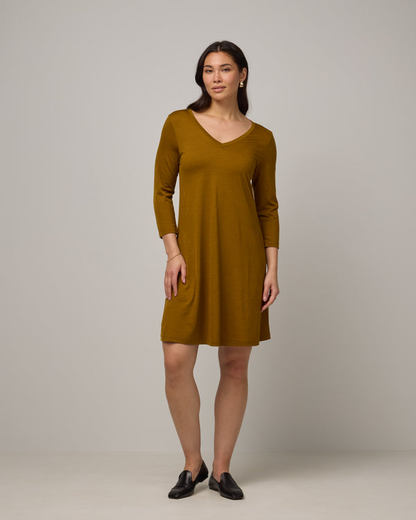 Model wearing Willow Swing Dress in Spiced Pear, a dark mustard color. Willow Swing Dress is a merino wool long sleeve, v-neck, knee length swing dress with pockets available in sizes XS-3X Regular, XS-3X Long.