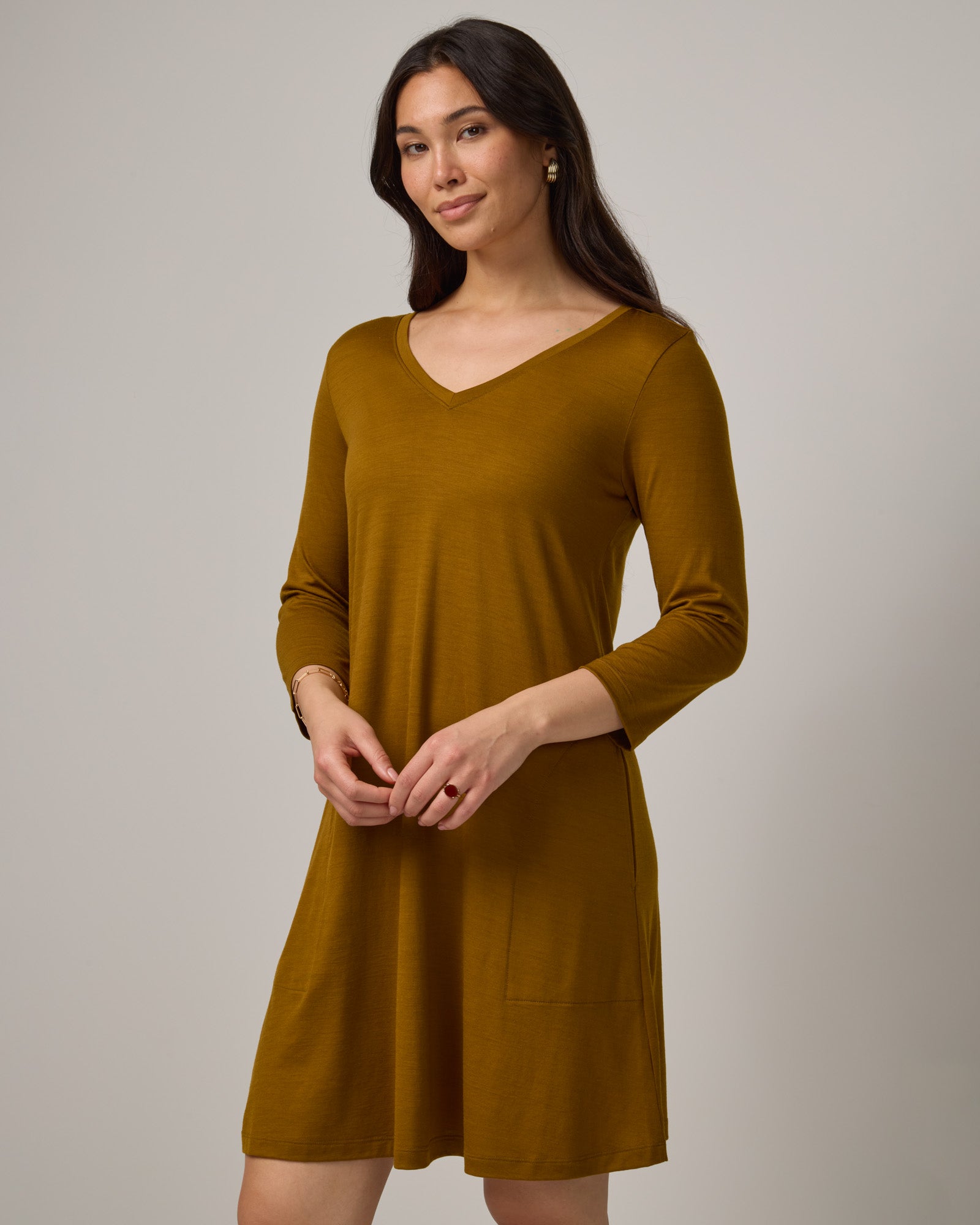Model wearing Willow Swing Dress in Spiced Pear, a dark mustard color. Willow Swing Dress is a merino wool long sleeve, v-neck, knee length swing dress with pockets available in sizes XS-3X Regular, XS-3X Long.