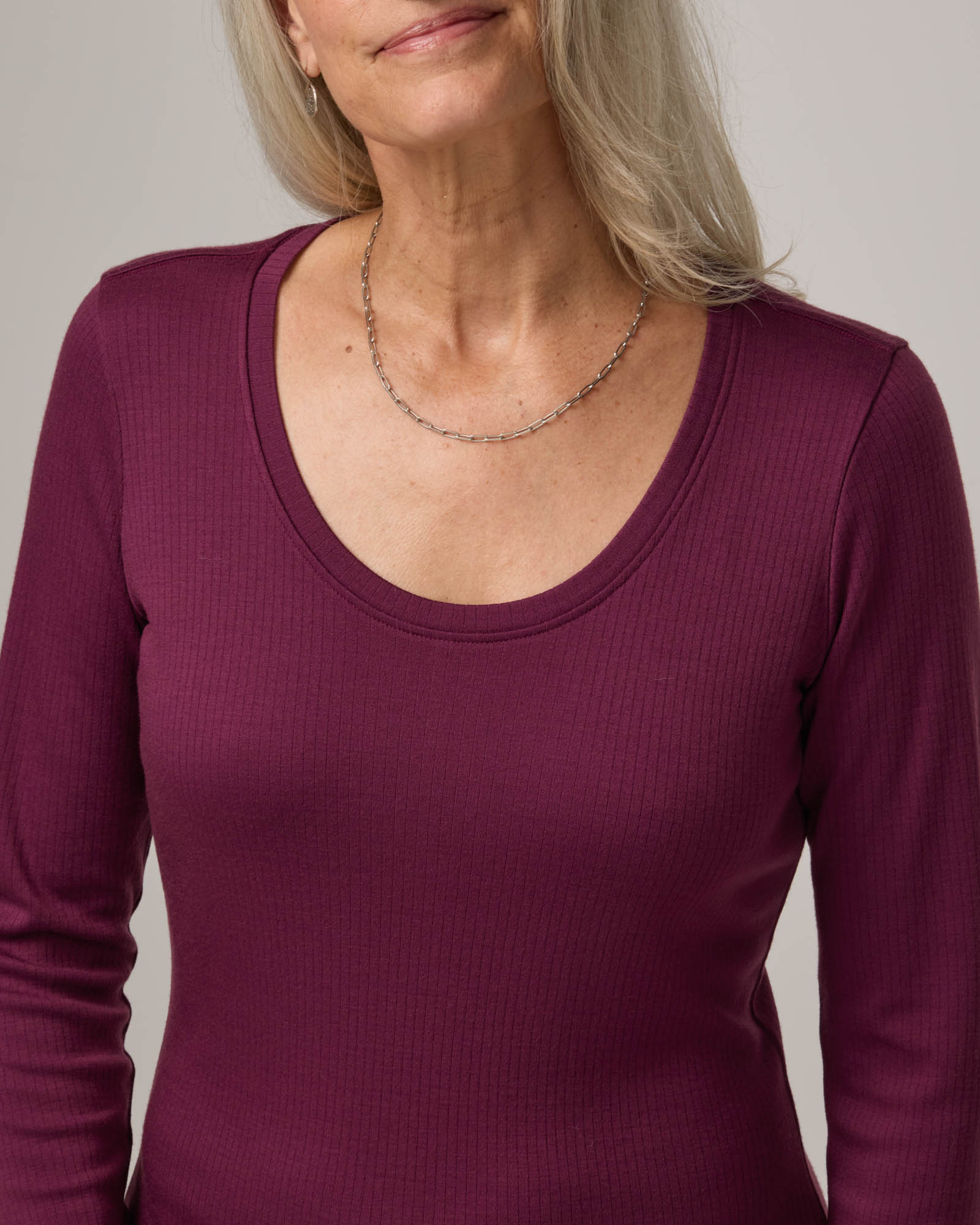 Model wearing Lex Ribbed Dress in Plum, a reddish-purple color. Lex Ribbed Dress is a merino wool long sleeve, scoop neck, fitted midi dress available in sizes XS-XXL Regular & XS-XL Petite.