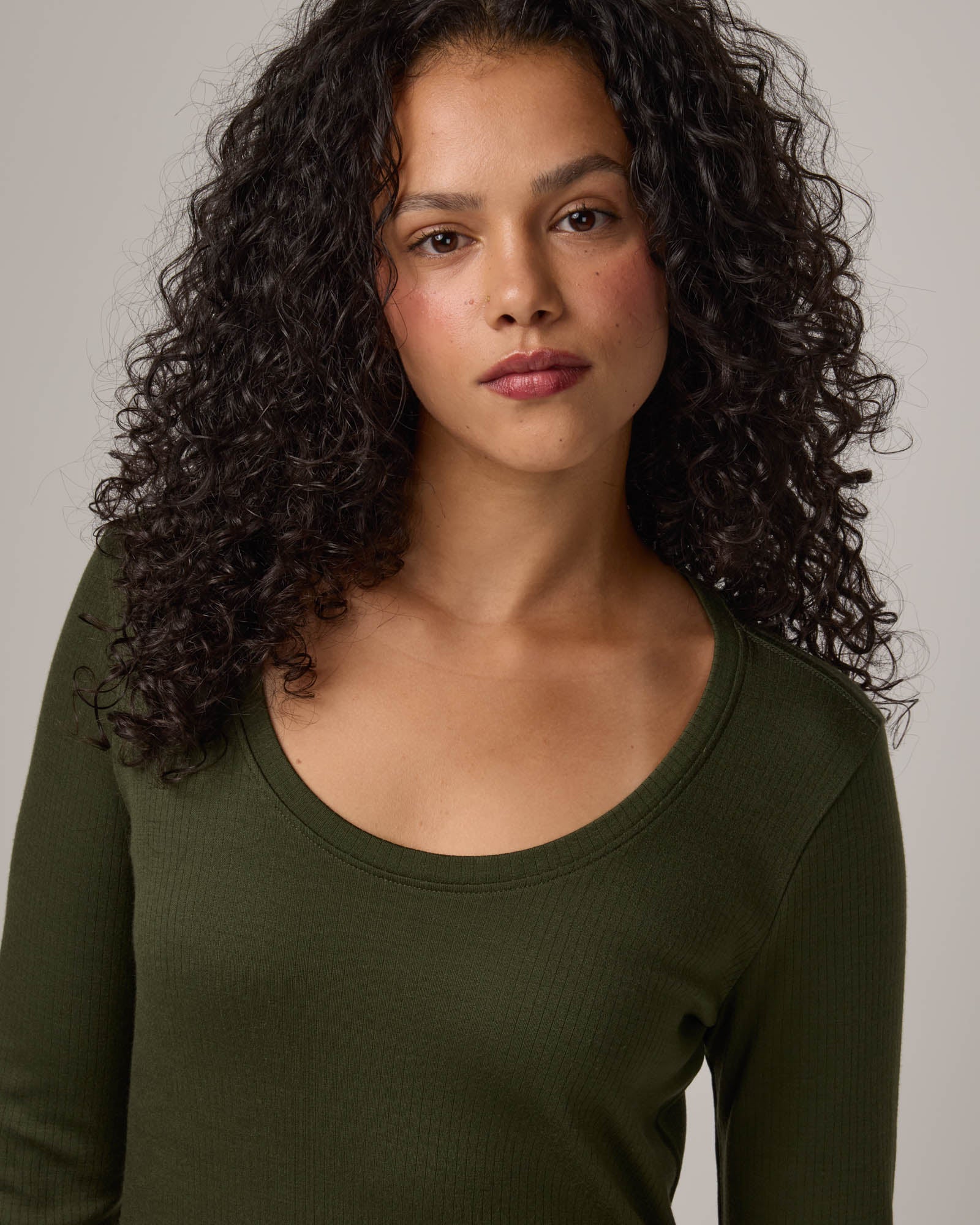 Model wearing Lex Ribbed Dress in Forest Night, a dark forest green color. Lex Ribbed Dress is a merino wool long sleeve, scoop neck, fitted midi dress available in sizes XS-XXL Regular & XS-XL Petite.