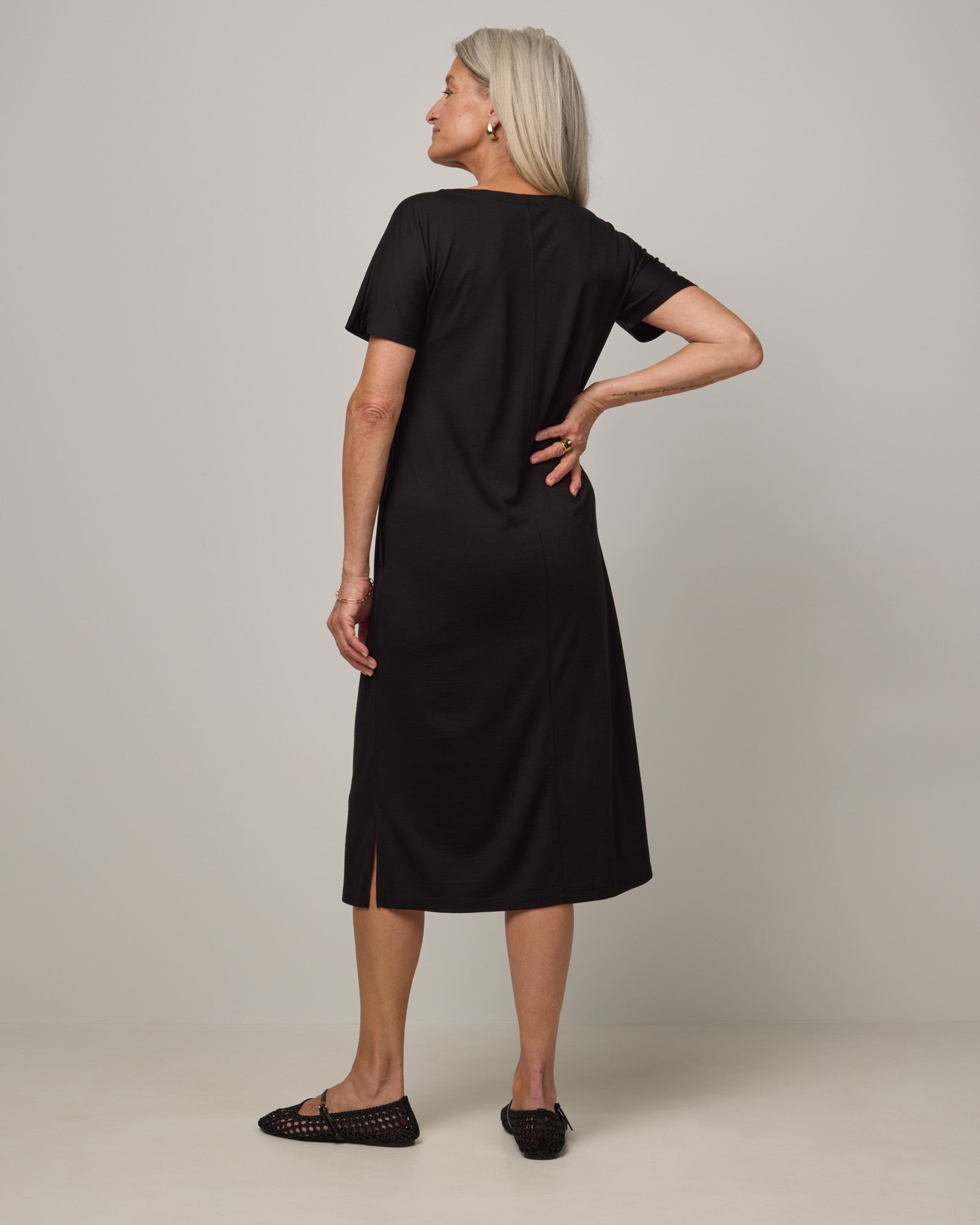 Model wearing Cora Shift Dress in Black. Cora Shift Dress is a merino wool short sleeve, midi shift dress with pockets and removable belt available in sizes XS-3X.