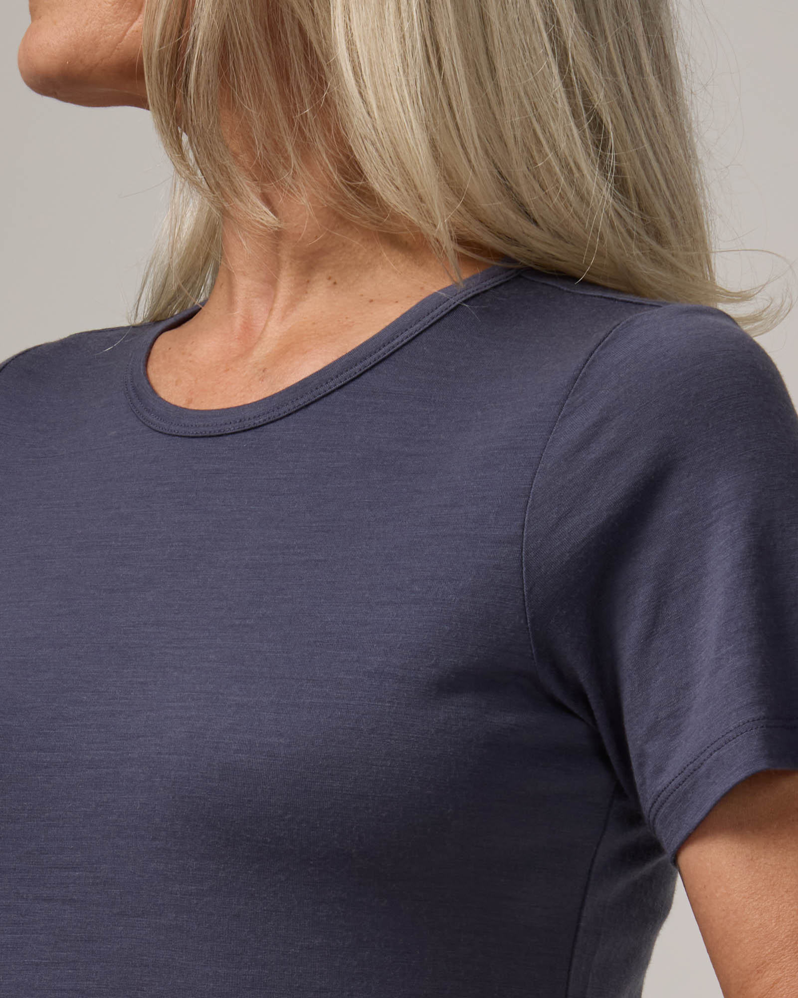 Model wearing Cara 100% Wool Fitted Tee in Odyssey Gray, a slate blue-gray color. Cara 100% Wool Fitted Tee is a merino wool short sleeve, crew neck, slim fit tee available in sizes XS-3X.