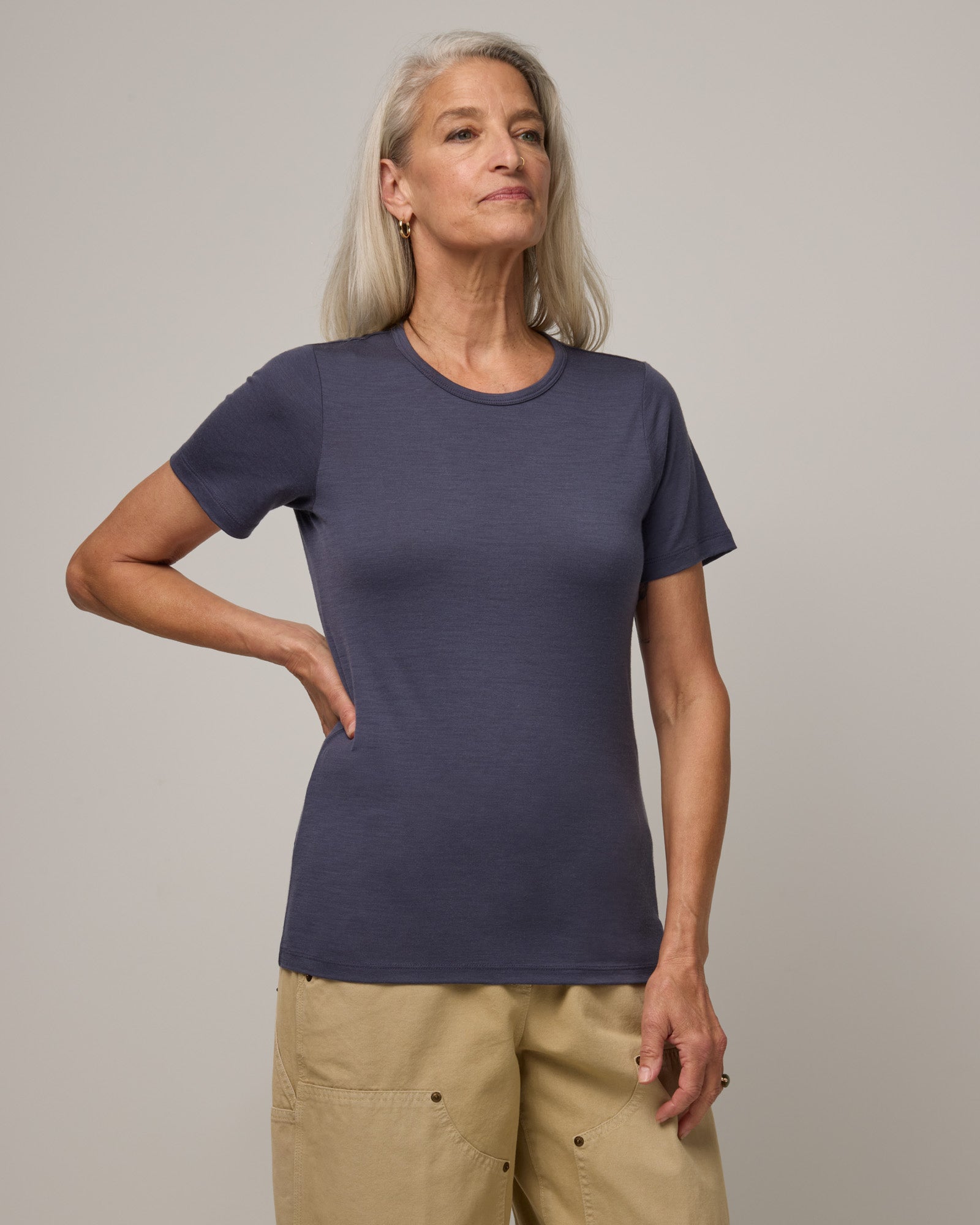 Model wearing Cara 100% Wool Fitted Tee in Odyssey Gray, a slate blue-gray color. Cara 100% Wool Fitted Tee is a merino wool short sleeve, crew neck, slim fit tee available in sizes XS-3X.