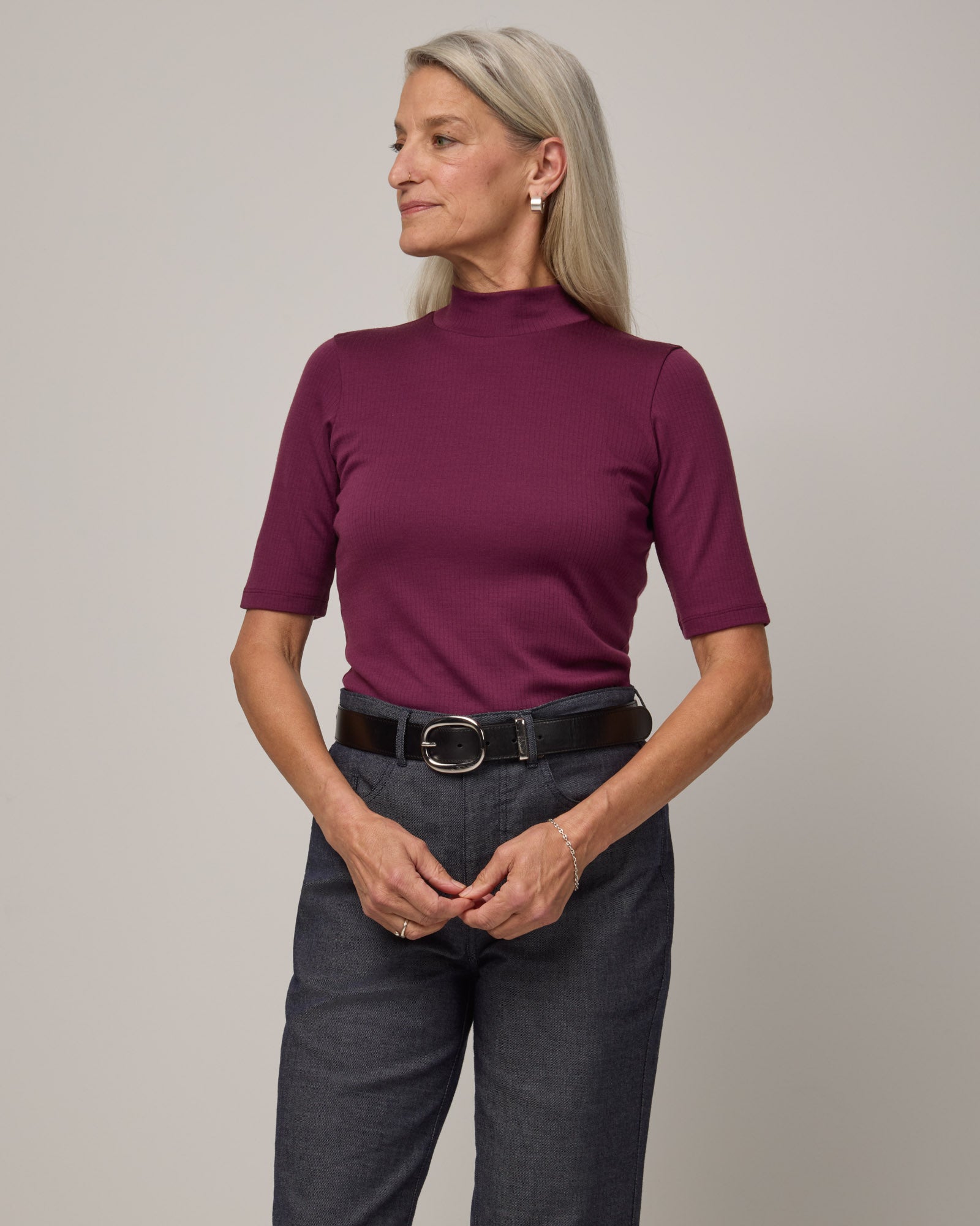 Model wearing Krystal Mock Neck Top in Plum, a reddish-purple color. Krystal Mock Neck Top is a merino wool half-sleeve, mock-neck ribbed tee available in sizes XS-XXL.