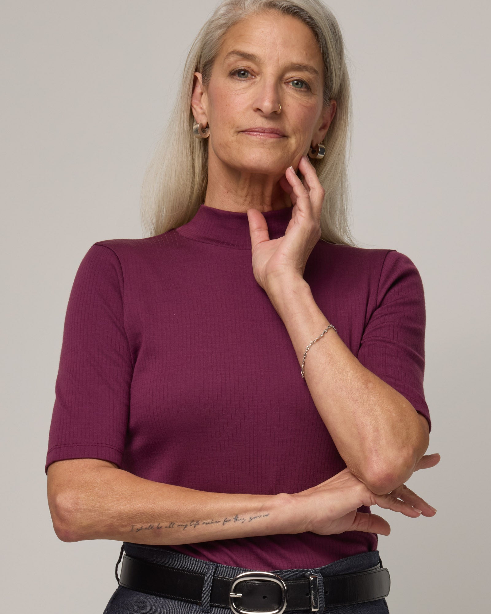 Model wearing Krystal Mock Neck Top in Plum, a reddish-purple color. Krystal Mock Neck Top is a merino wool half-sleeve, mock-neck ribbed tee available in sizes XS-XXL.