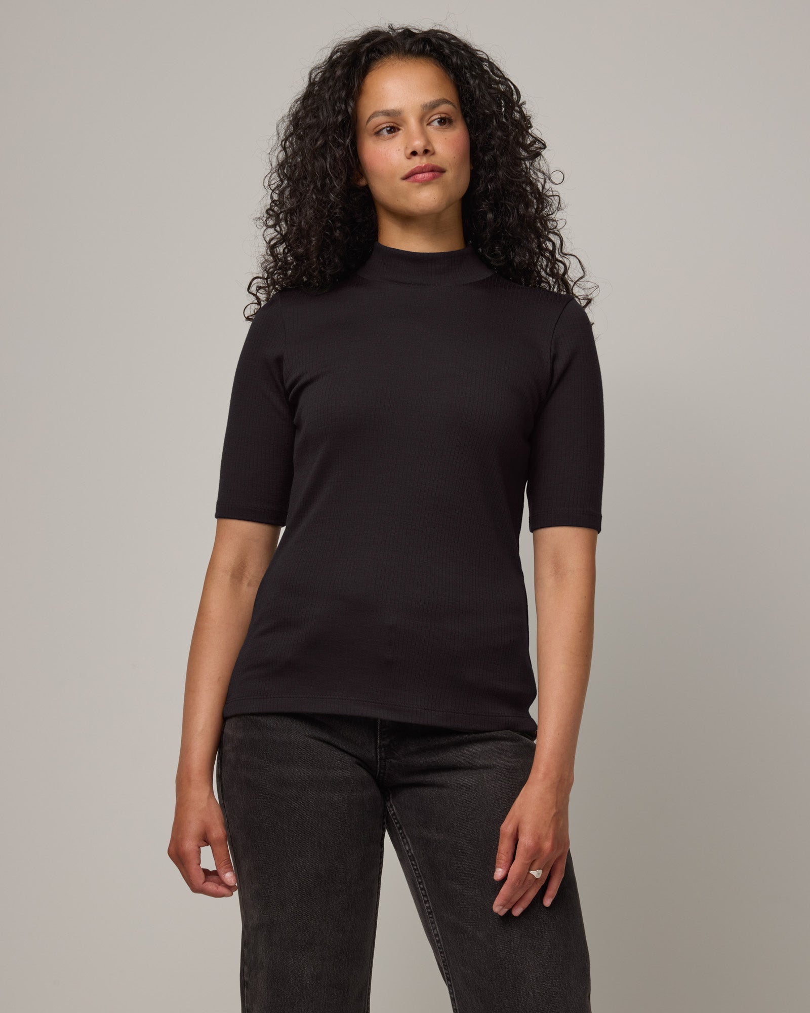 Model wearing Krystal Mock Neck Top in Black. Krystal Mock Neck Top is a merino wool half-sleeve, mock-neck ribbed tee available in sizes XS-XXL.