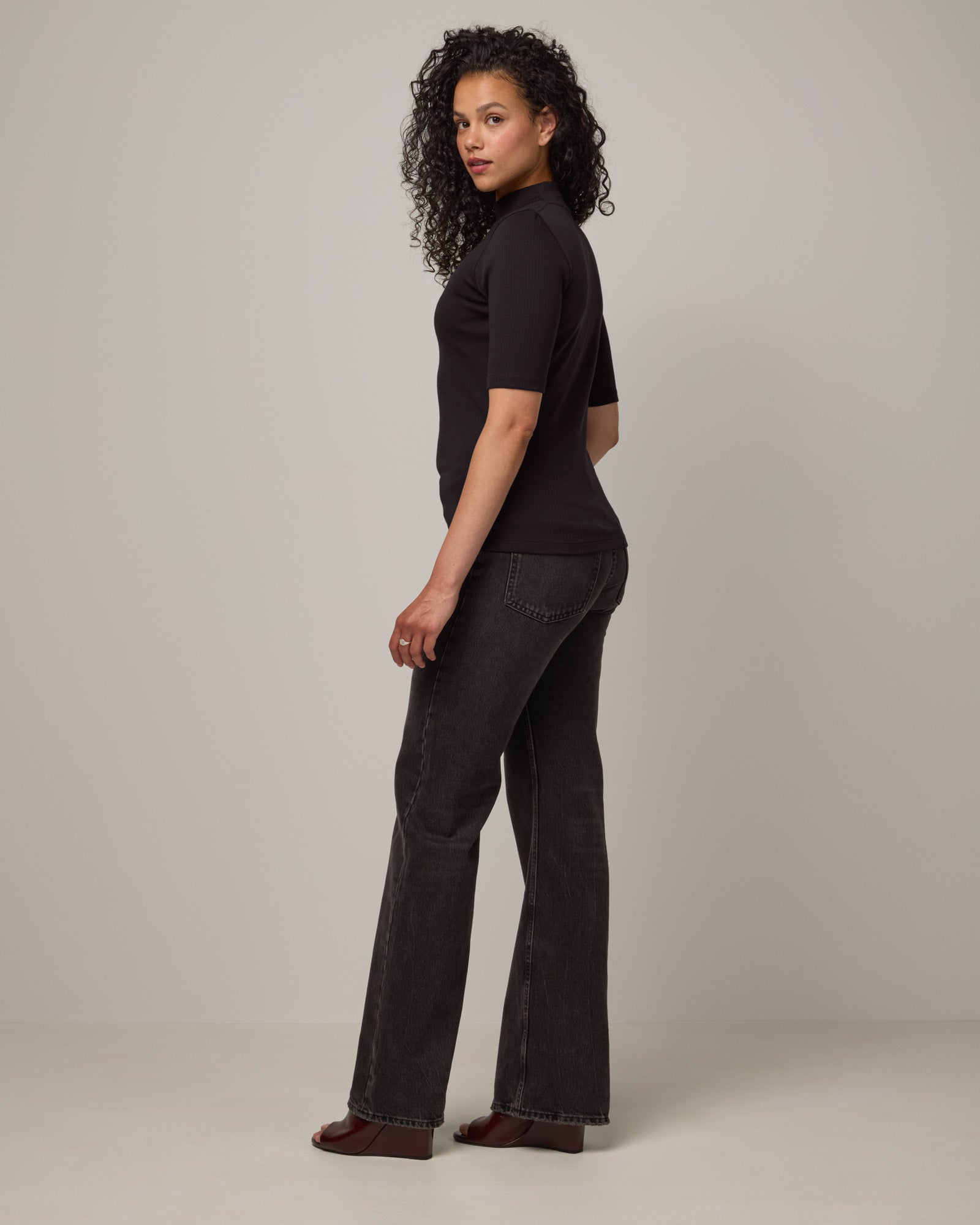 Model wearing Krystal Mock Neck Top in Black. Krystal Mock Neck Top is a merino wool half-sleeve, mock-neck ribbed tee available in sizes XS-XXL.