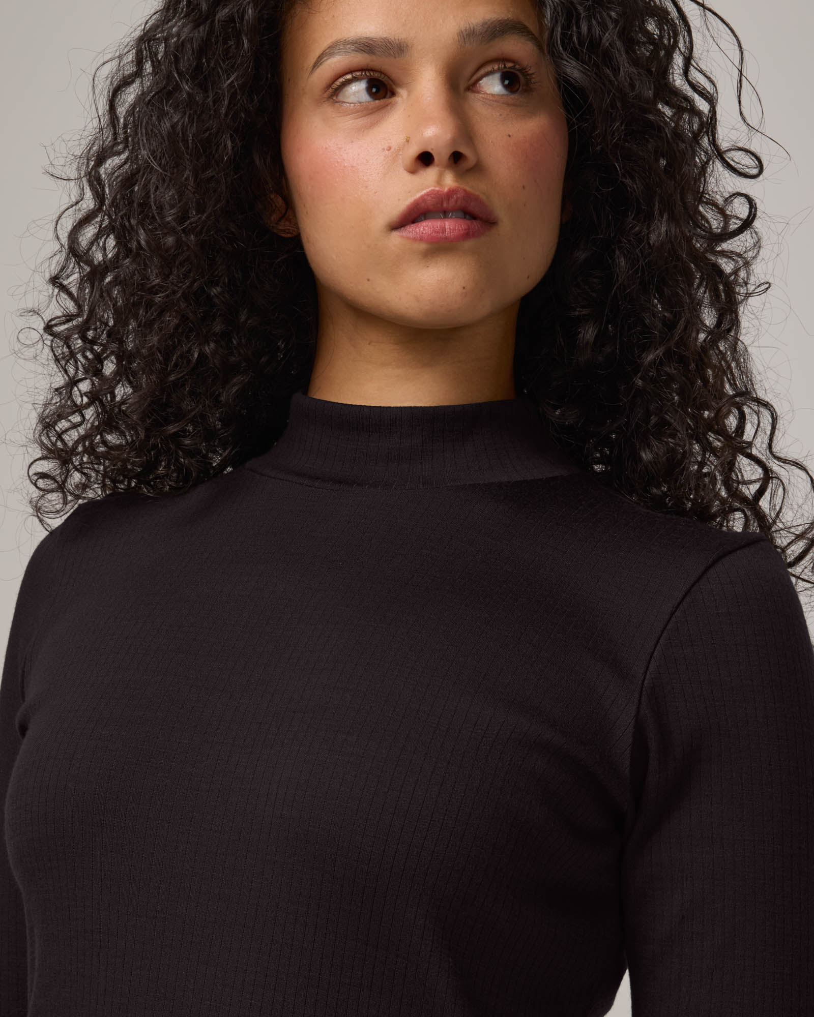 Model wearing Krystal Mock Neck Top in Black. Krystal Mock Neck Top is a merino wool half-sleeve, mock-neck ribbed tee available in sizes XS-XXL.