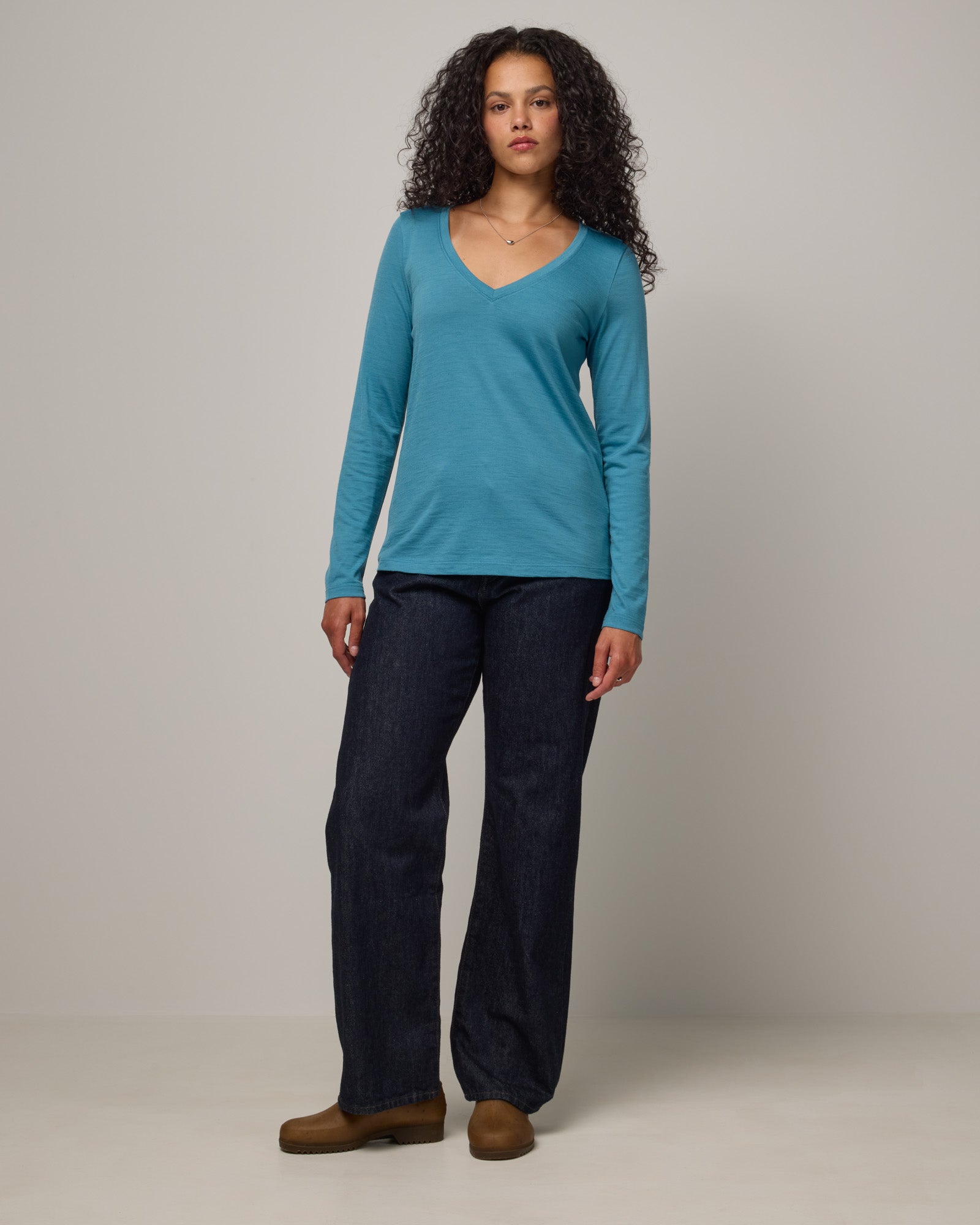 Model wearing Brenton V-Neck Tee in Alpine Blue, a glacier ice blue color. Brenton V-Neck Tee is a merino wool long sleeve, v-neck, regular fit tee available in sizes XS-3X.
