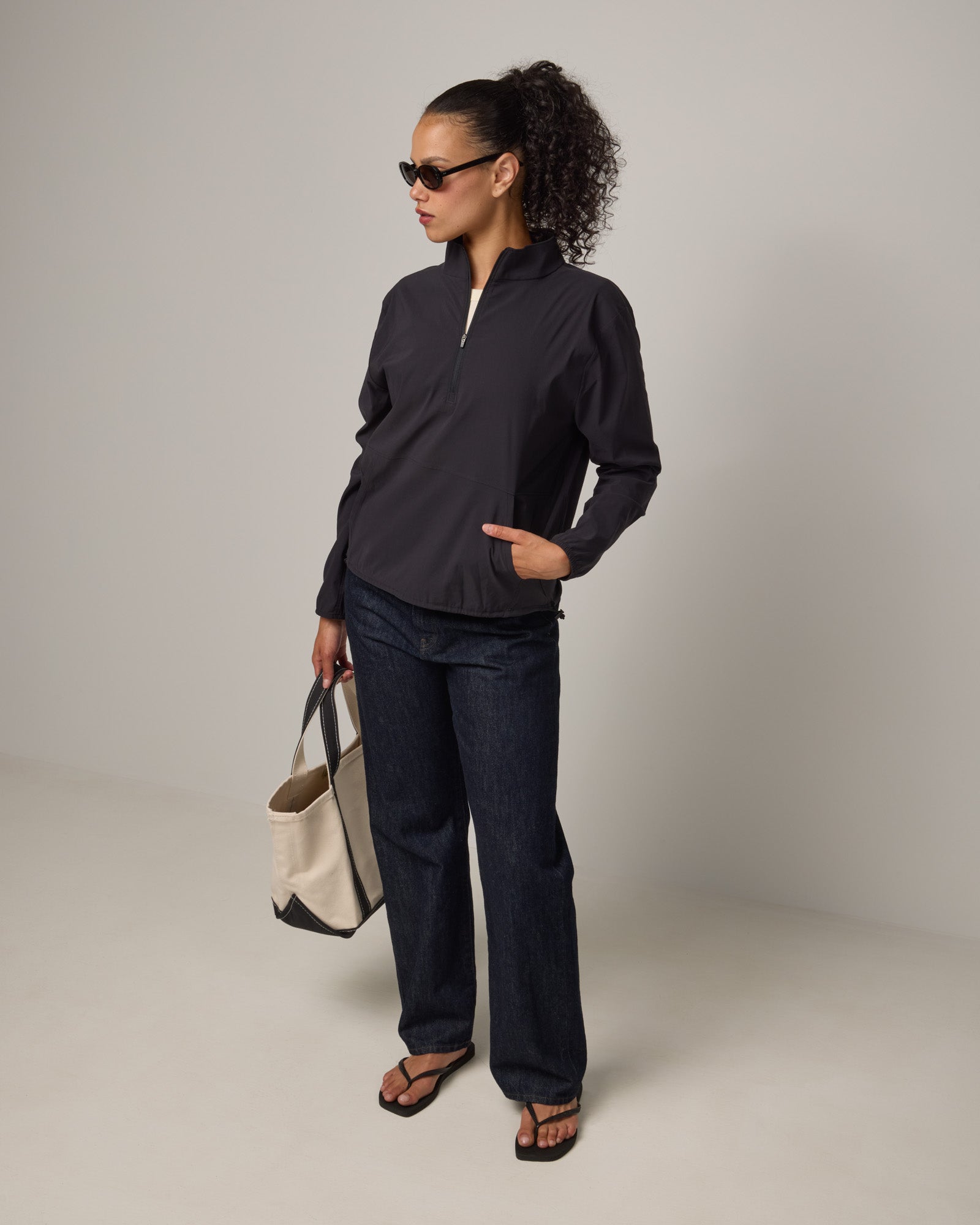 Model wearing Venus Quarter Zip in Black. Venus Quarter Zip is a merino wool lightweight long sleeve pullover with a front pocket available in sizes XS-XXL. 