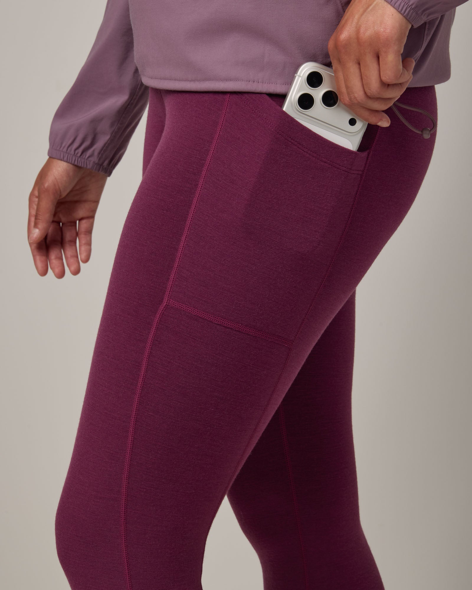 Model wearing Summit Pocket Legging in Plum, a reddish-purple color. Summit Pocket Legging is a merino wool legging with pockets available in sizes XS-3X Regular, S-XXL Long.