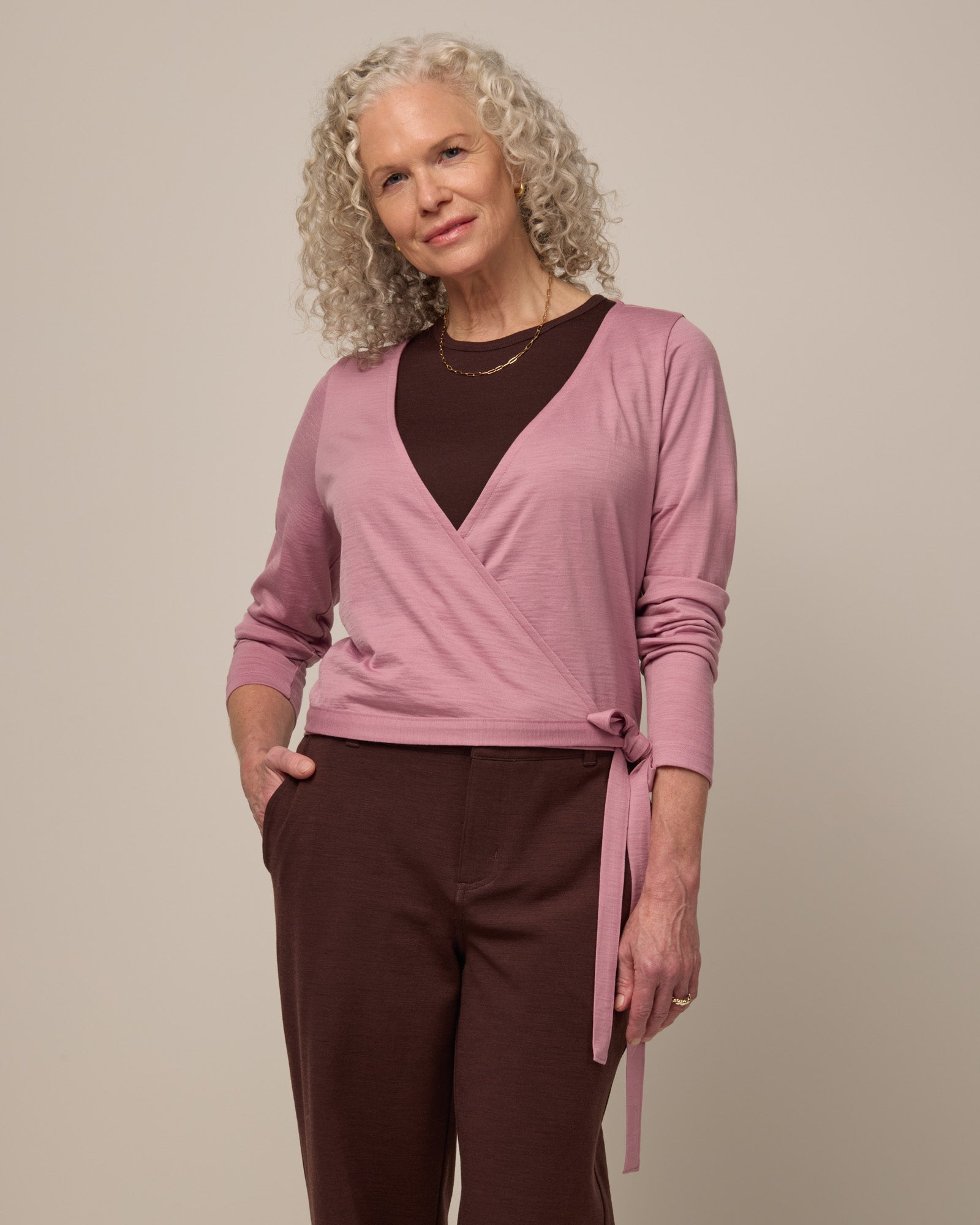 Model wearing Natalia Wrap Top in Ballet Pink, a muted light pink color. Natalia Wrap Top is a merino wool long sleeve, v-neck, slim fit top available in sizes XS-3X.