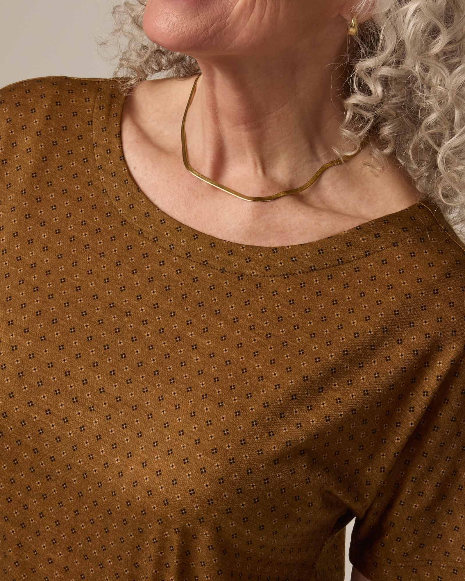 Model wearing Cora Shift Dress in Geo Stamp Print, a dainty, neutral, geometric print on a dark ochre background. Cora Shift Dress is a merino wool short sleeve, midi shift dress with pockets and removable belt available in sizes XS-3X.