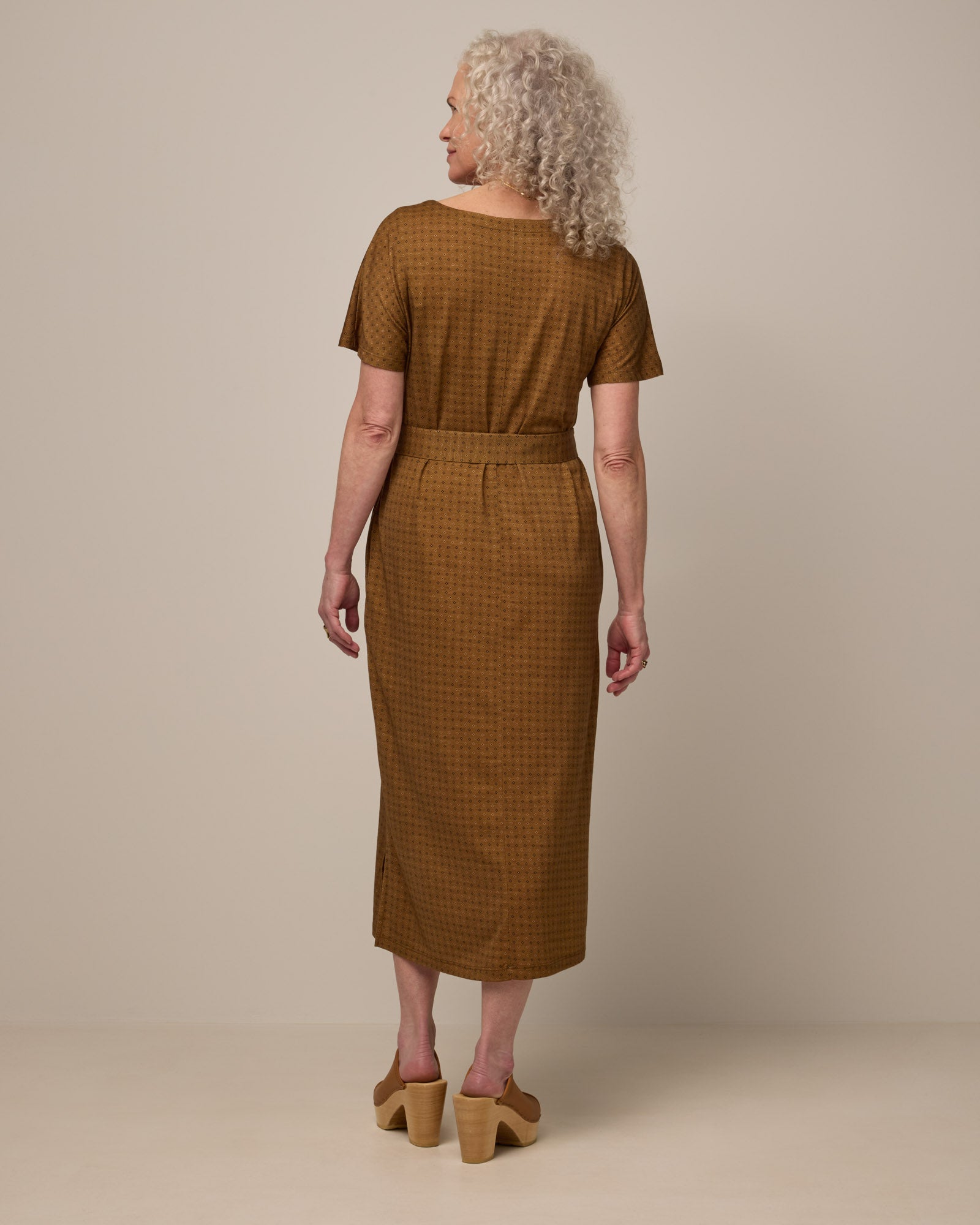 Model wearing Cora Shift Dress in Geo Stamp Print, a dainty, neutral, geometric print on a dark ochre background. Cora Shift Dress is a merino wool short sleeve, midi shift dress with pockets and removable belt available in sizes XS-3X.