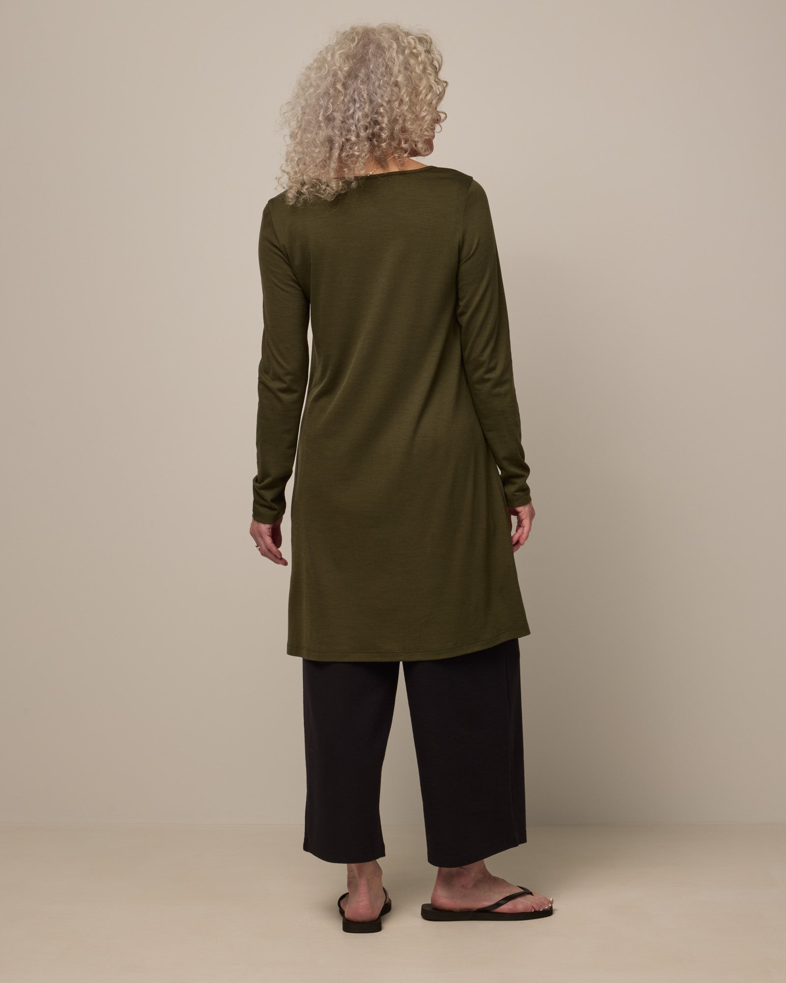 Model wearing Rowena Swing Dress in Forest Night, a dark forest green color. Rowena Swing Dress is a merino wool long sleeve, boatneck, knee length swing dress with pockets available in sizes XS-3X Regular, XS-3X Long.