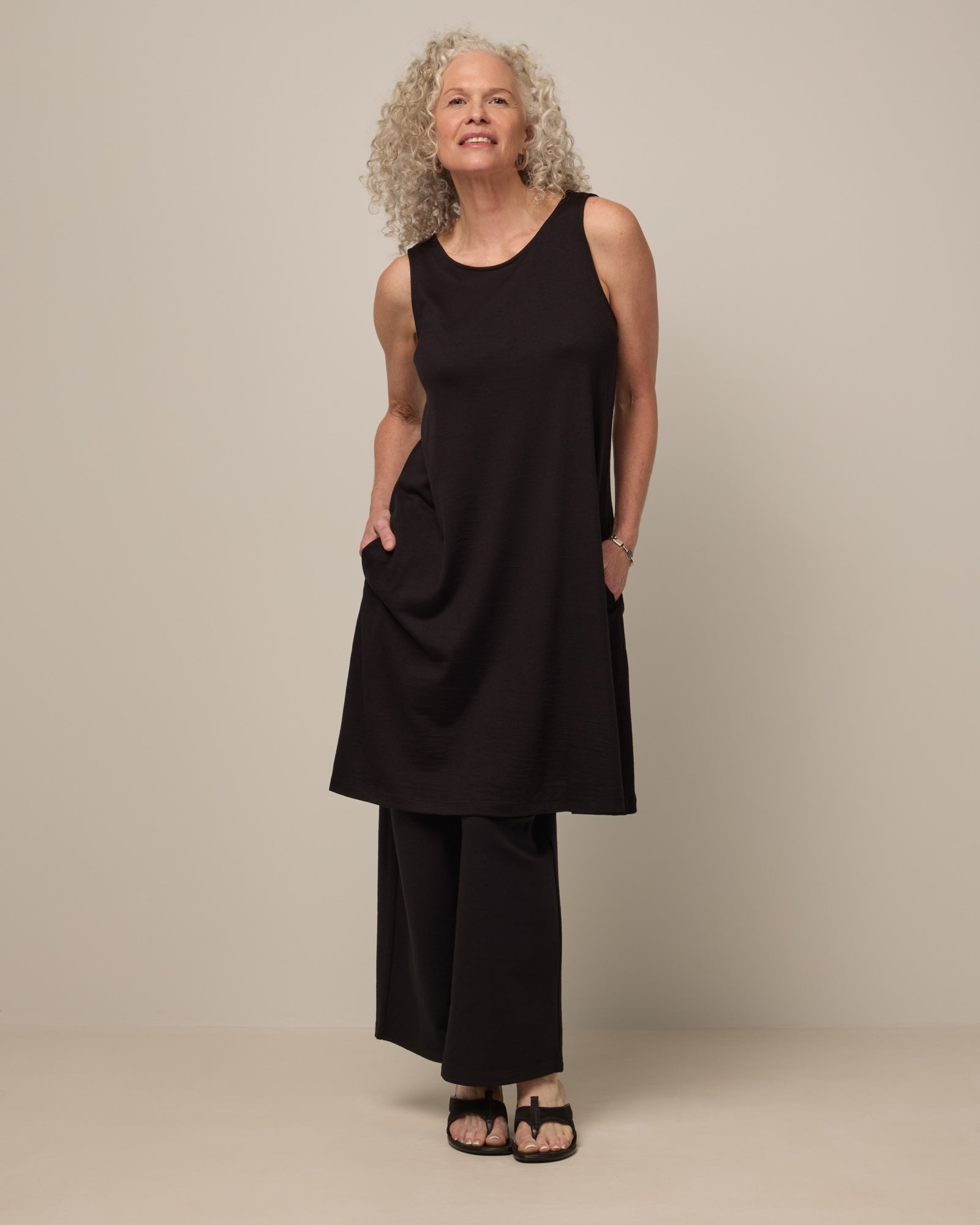 Model wearing Camellia Tank Dress in Black. Camellia Tank Dress is a merino wool sleeveless, crew neck, knee length swing dress with pockets available in sizes XS-3X Regular, XS-3X Long.