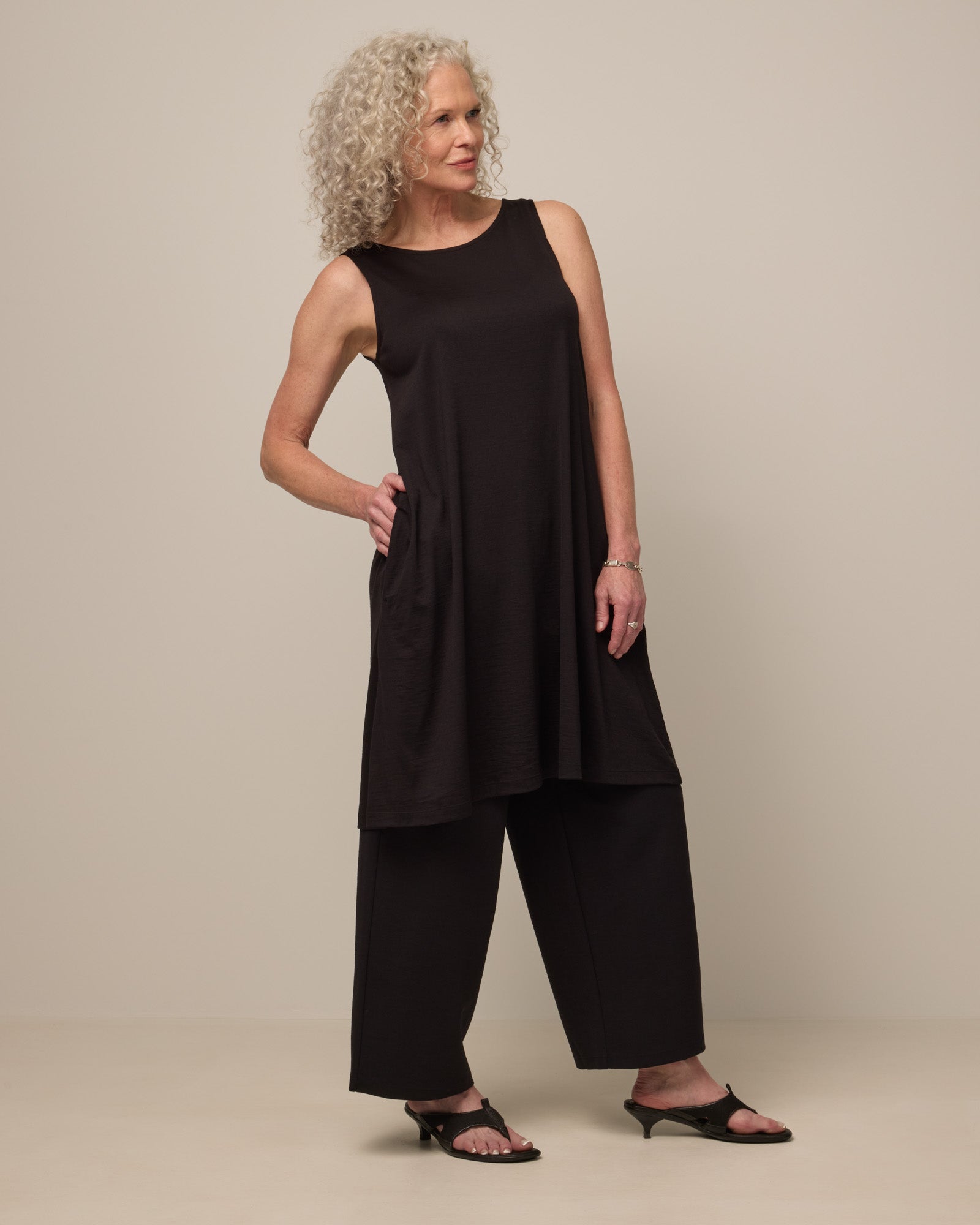 Model wearing Camellia Tank Dress in Black. Camellia Tank Dress is a merino wool sleeveless, crew neck, knee length swing dress with pockets available in sizes XS-3X Regular, XS-3X Long.