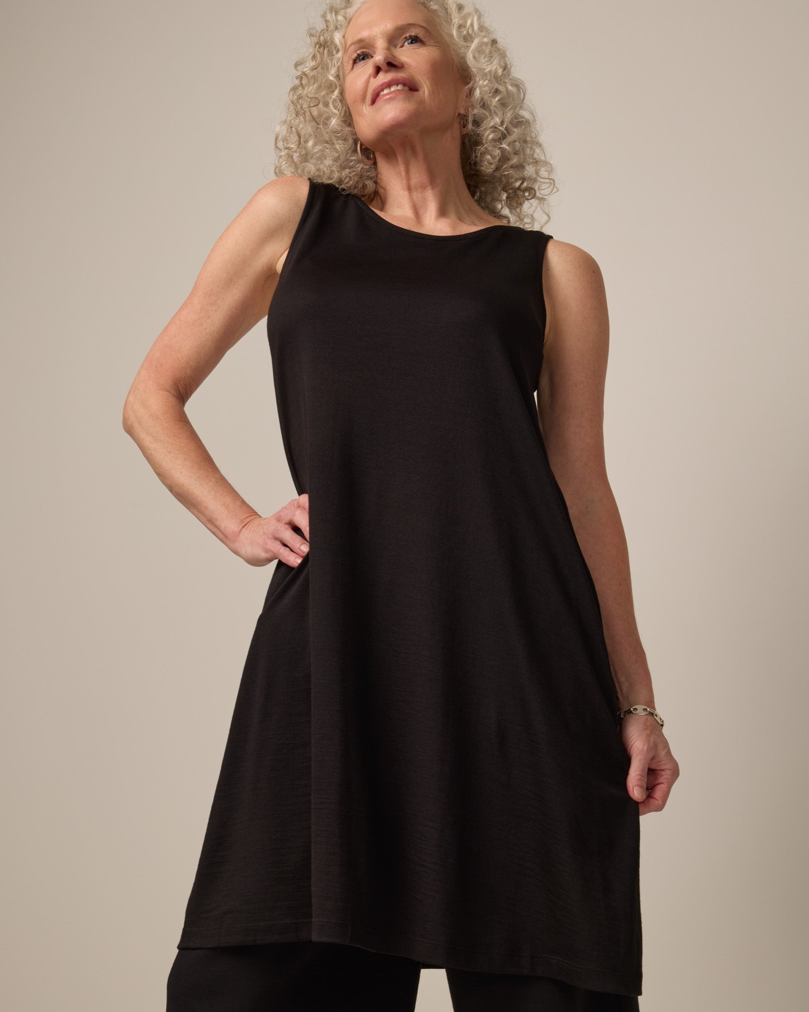Model wearing Camellia Tank Dress in Black. Camellia Tank Dress is a merino wool sleeveless, crew neck, knee length swing dress with pockets available in sizes XS-3X Regular, XS-3X Long.