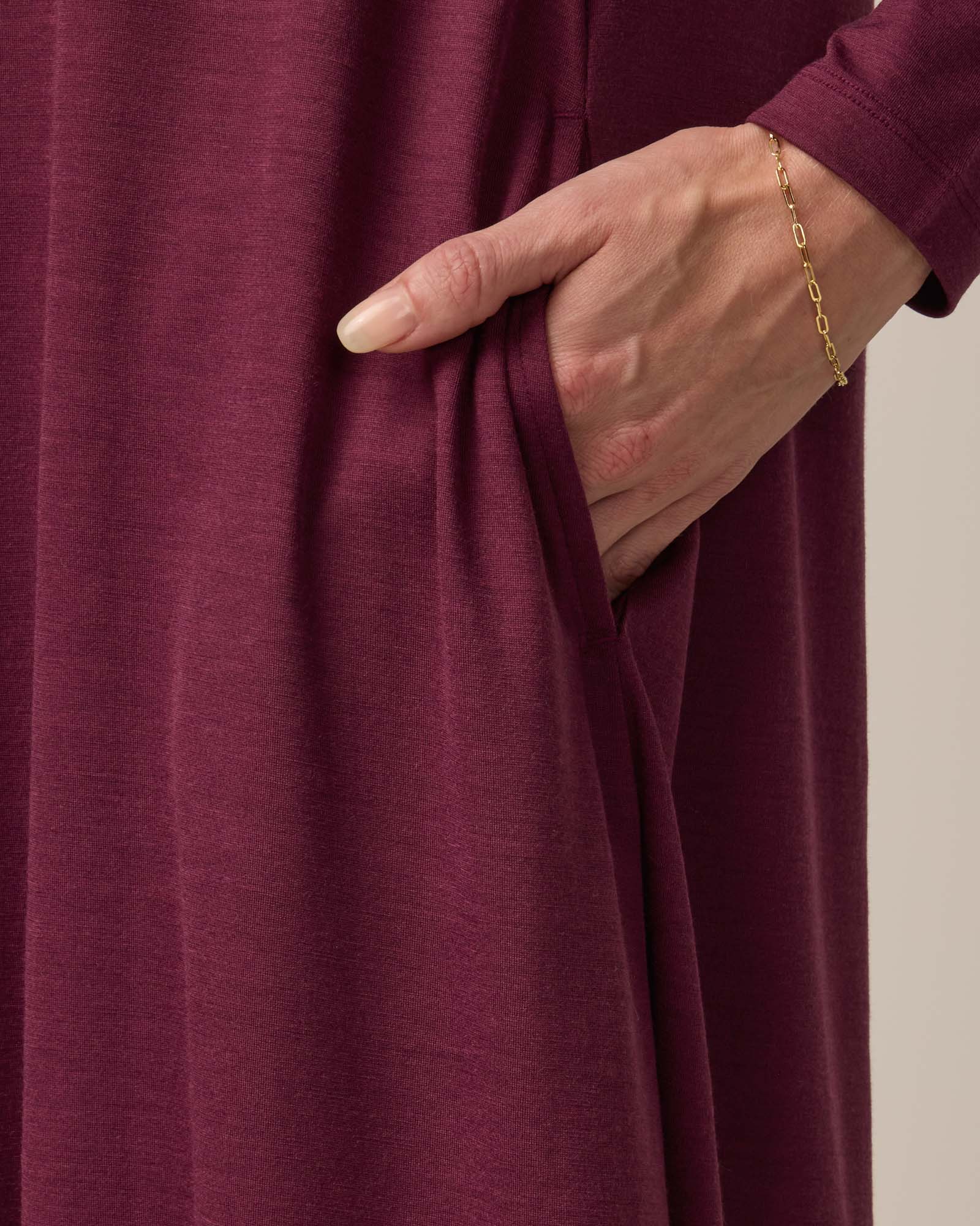 Model wearing Rowena Swing Dress in Plum, a reddish-purple color. Rowena Swing Dress is a merino wool long sleeve, boatneck, knee length swing dress with pockets available in sizes XS-3X Regular, XS-3X Long.