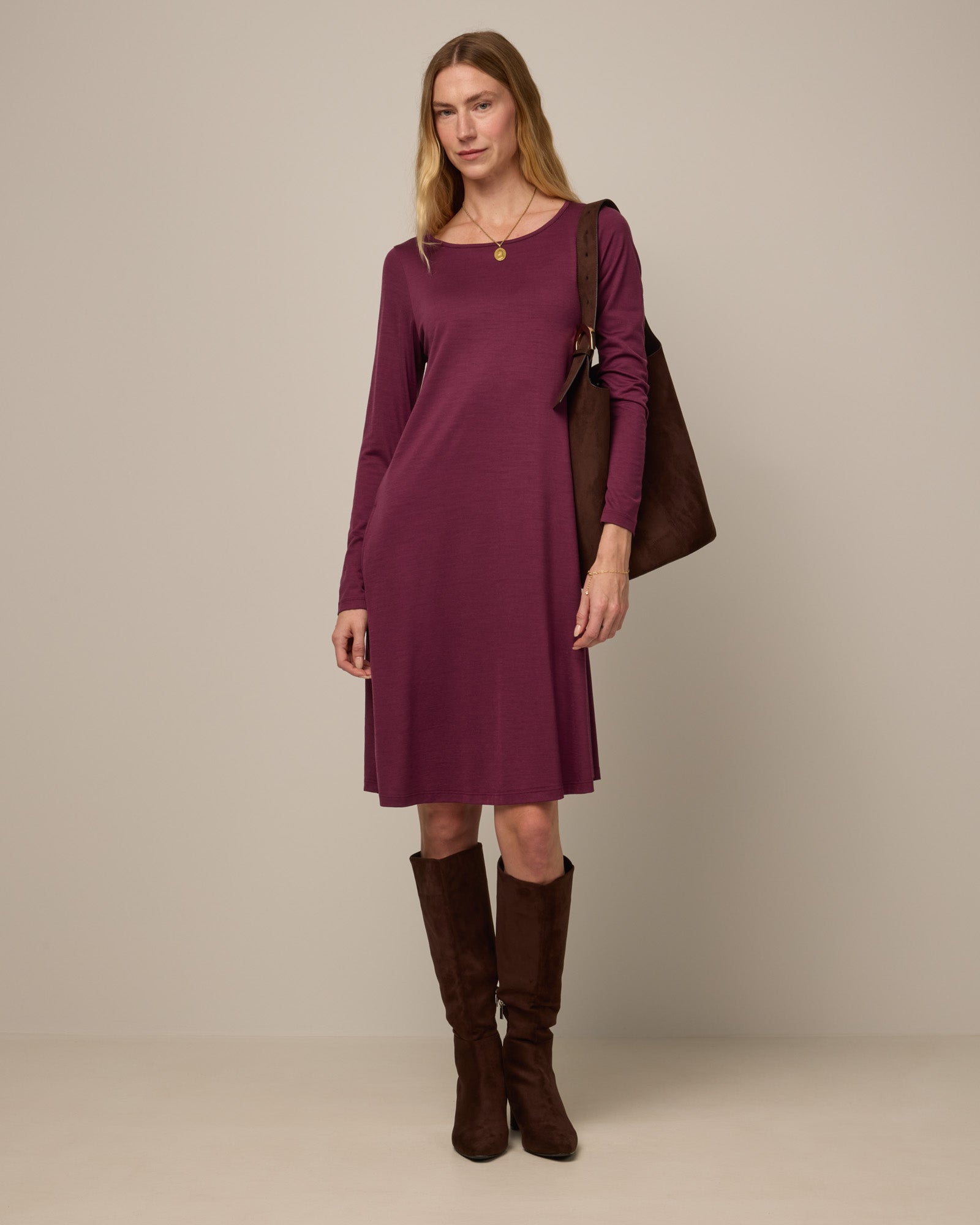 Model wearing Rowena Swing Dress in Plum, a reddish-purple color. Rowena Swing Dress is a merino wool long sleeve, boatneck, knee length swing dress with pockets available in sizes XS-3X Regular, XS-3X Long.