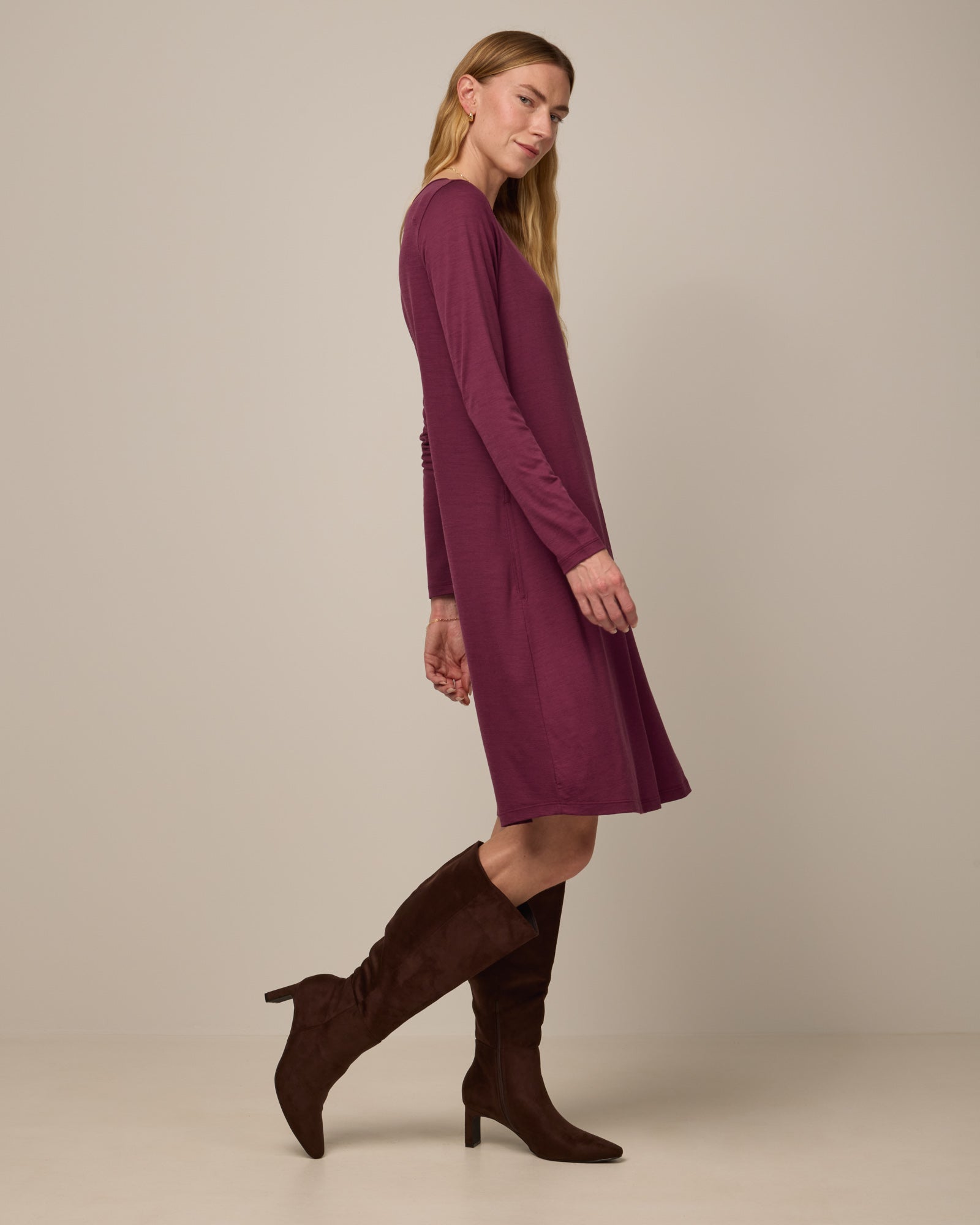 Model wearing Rowena Swing Dress in Plum, a reddish-purple color. Rowena Swing Dress is a merino wool long sleeve, boatneck, knee length swing dress with pockets available in sizes XS-3X Regular, XS-3X Long.