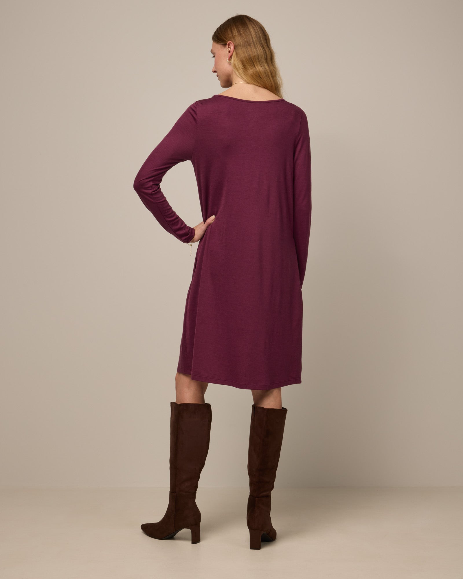 Model wearing Rowena Swing Dress in Plum, a reddish-purple color. Rowena Swing Dress is a merino wool long sleeve, boatneck, knee length swing dress with pockets available in sizes XS-3X Regular, XS-3X Long.