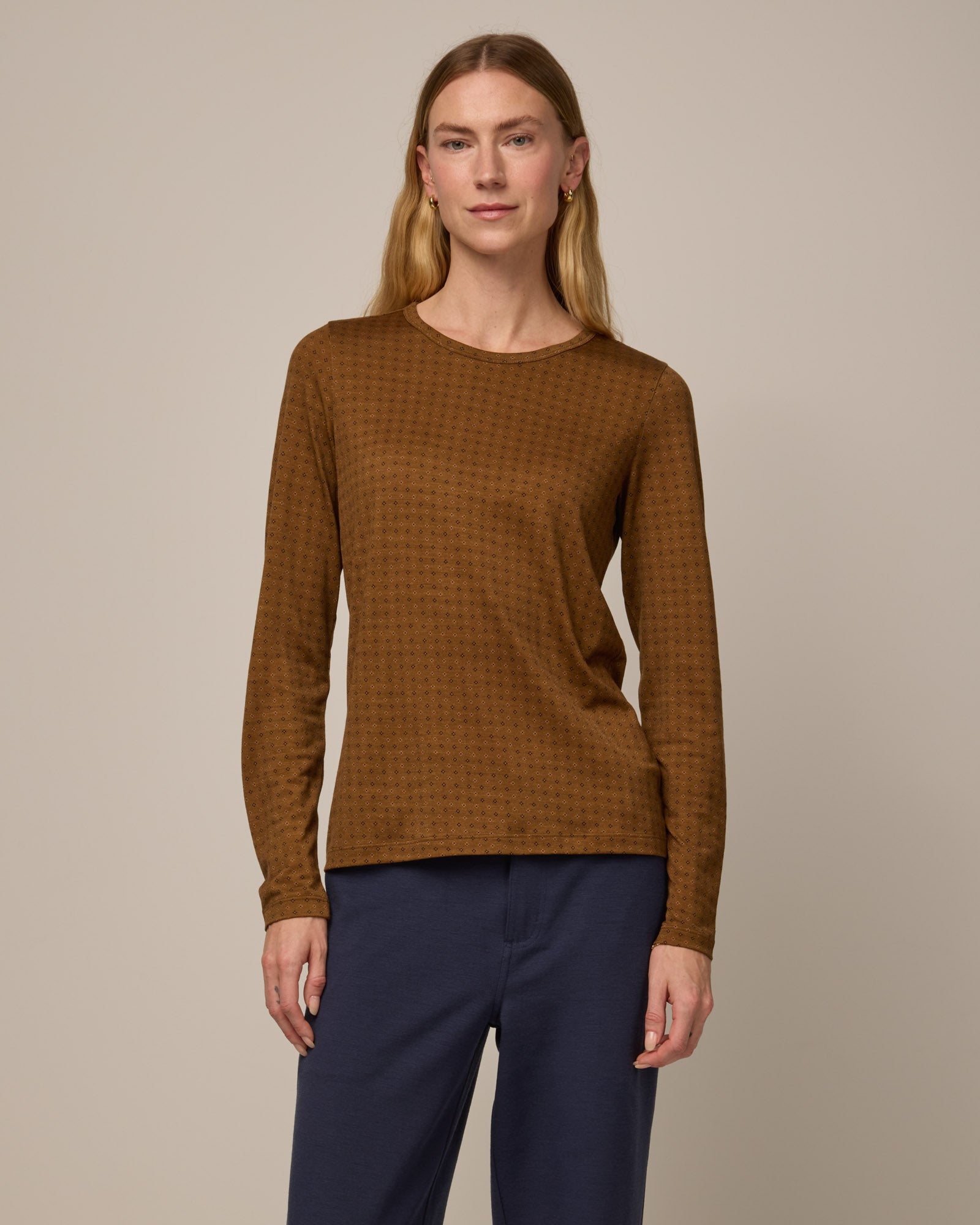 Model wearing Sloan Signature Fitted Tee in Geo Stamp Print, a dainty, neutral, geometric print on a dark ochre background. Sloan Signature Fitted Tee is a merino wool long sleeve, crew neck, slim fit tee available in sizes XS-3X.