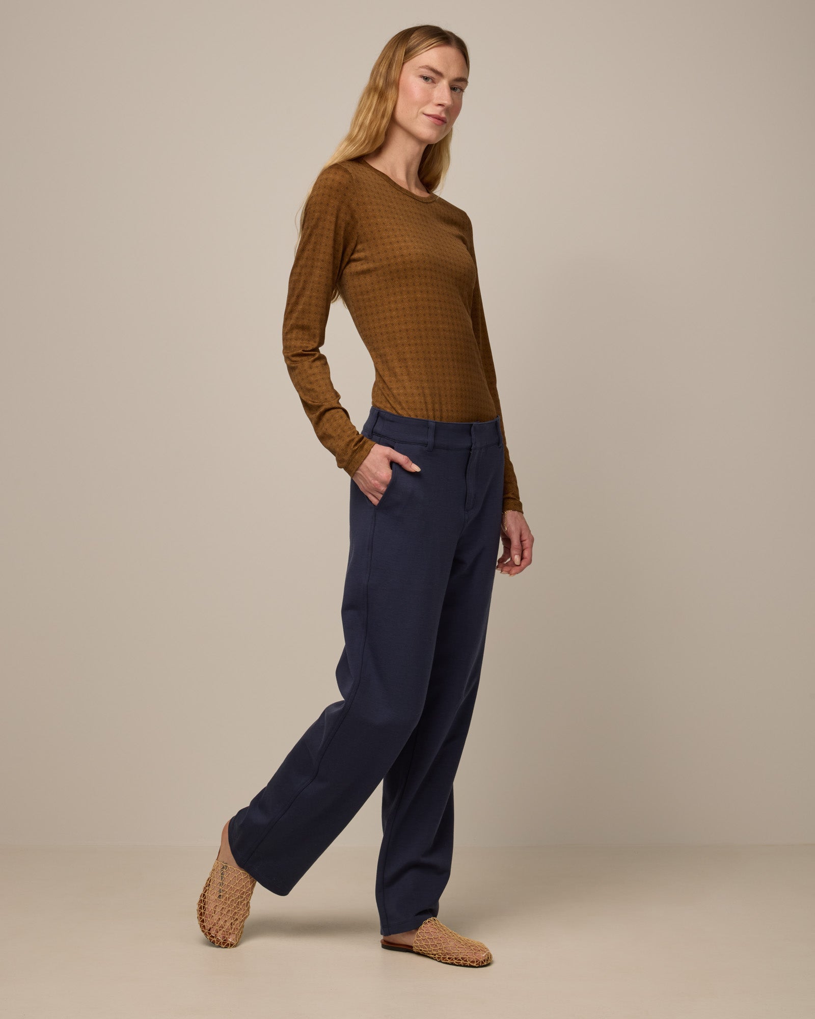 Model wearing Sloan Signature Fitted Tee in Geo Stamp Print, a dainty, neutral, geometric print on a dark ochre background. Sloan Signature Fitted Tee is a merino wool long sleeve, crew neck, slim fit tee available in sizes XS-3X.