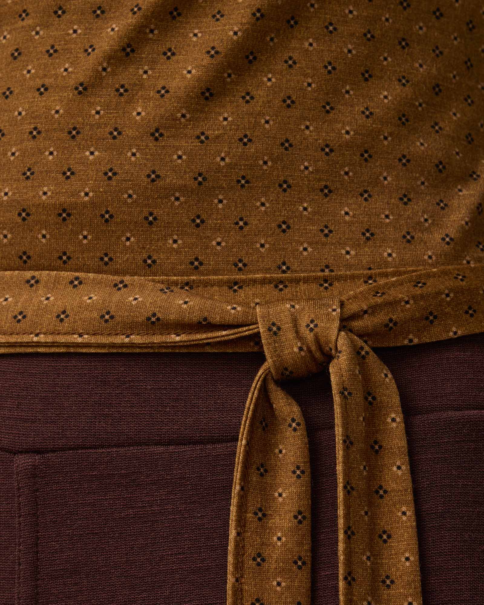 Detail of Natalia Wrap Top in Geo Stamp Print, a dainty, neutral, geometric print on a dark ochre background. Natalia Wrap Top is a merino wool long sleeve, v-neck, slim fit top available in sizes XS-3X.