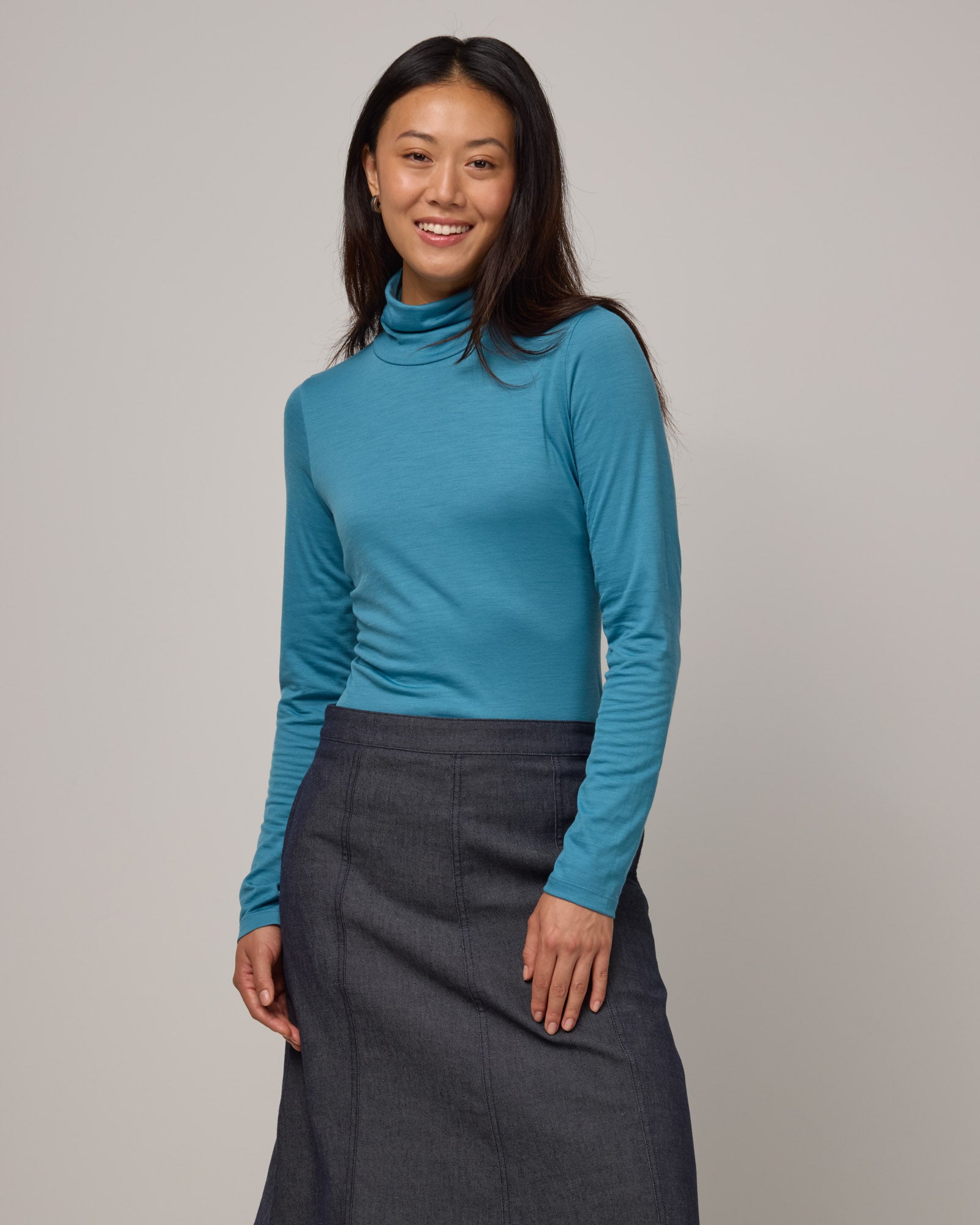 Model wearing Addison Turtleneck Top in Alpine Blue, a glacier ice blue color. Addison Turtleneck Top is a merino wool long sleeve, turtleneck, slim fit top available in sizes XS-3X.