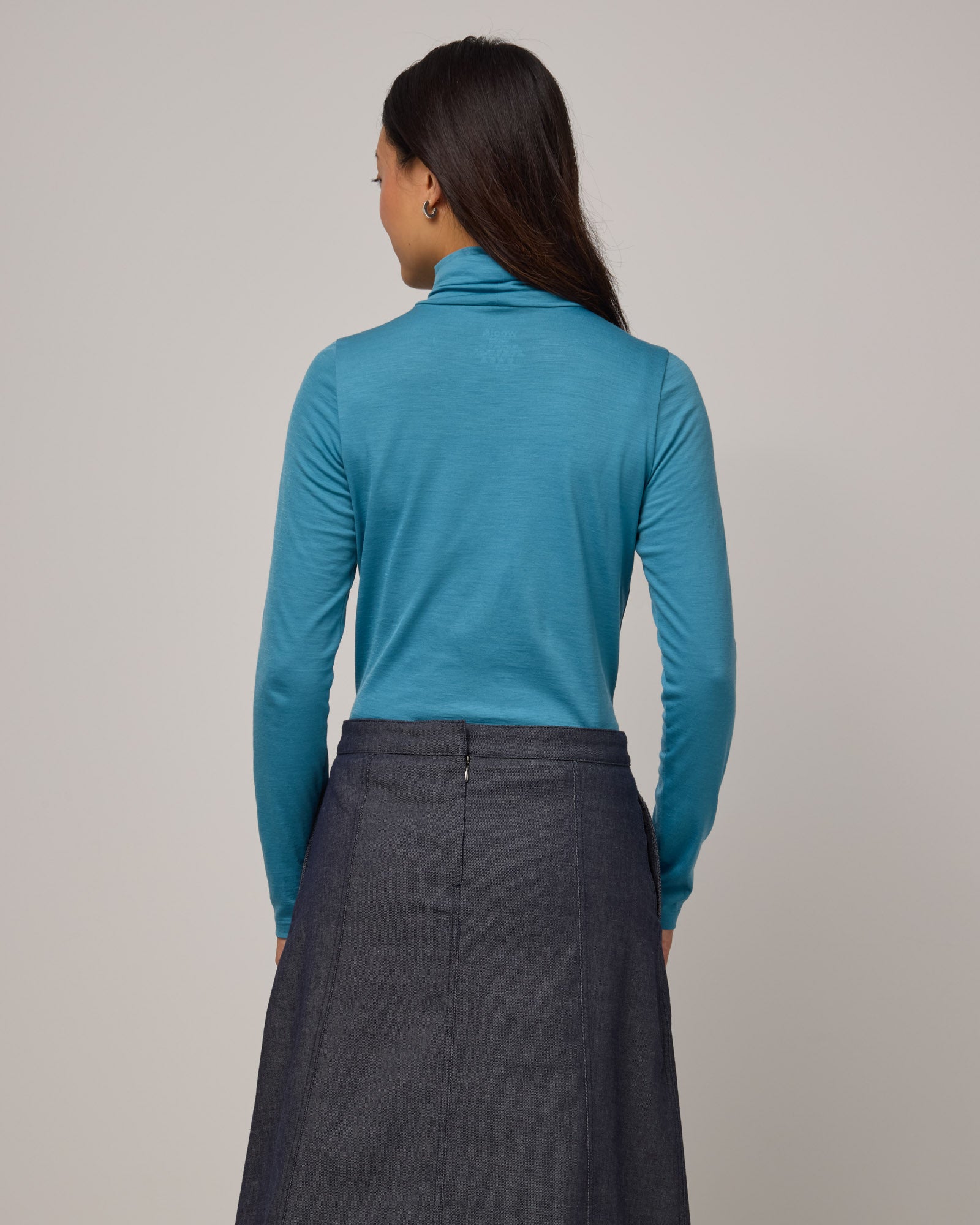 Model wearing Addison Turtleneck Top in Alpine Blue, a glacier ice blue color. Addison Turtleneck Top is a merino wool long sleeve, turtleneck, slim fit top available in sizes XS-3X.