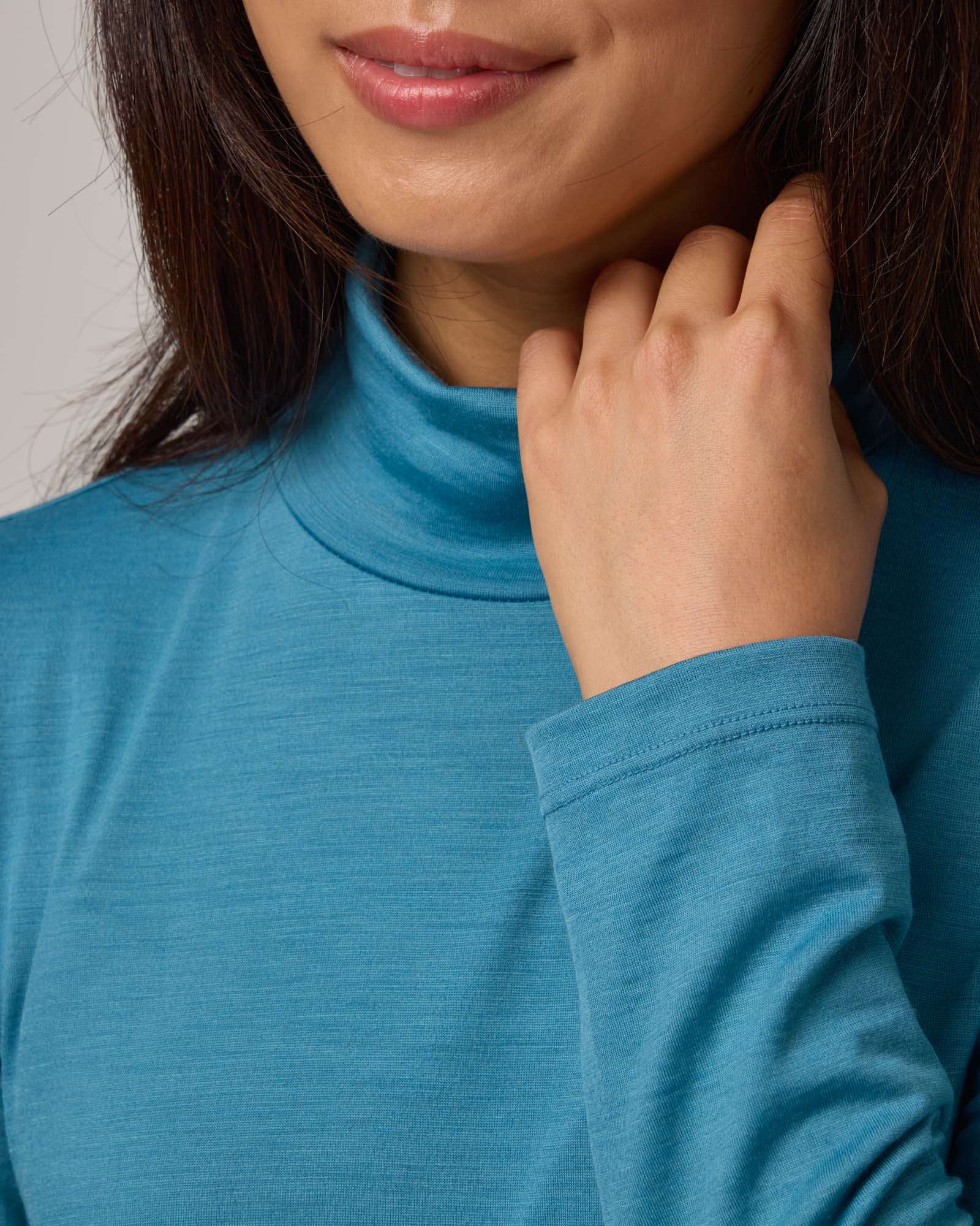 Model wearing Addison Turtleneck Top in Alpine Blue, a glacier ice blue color. Addison Turtleneck Top is a merino wool long sleeve, turtleneck, slim fit top available in sizes XS-3X.