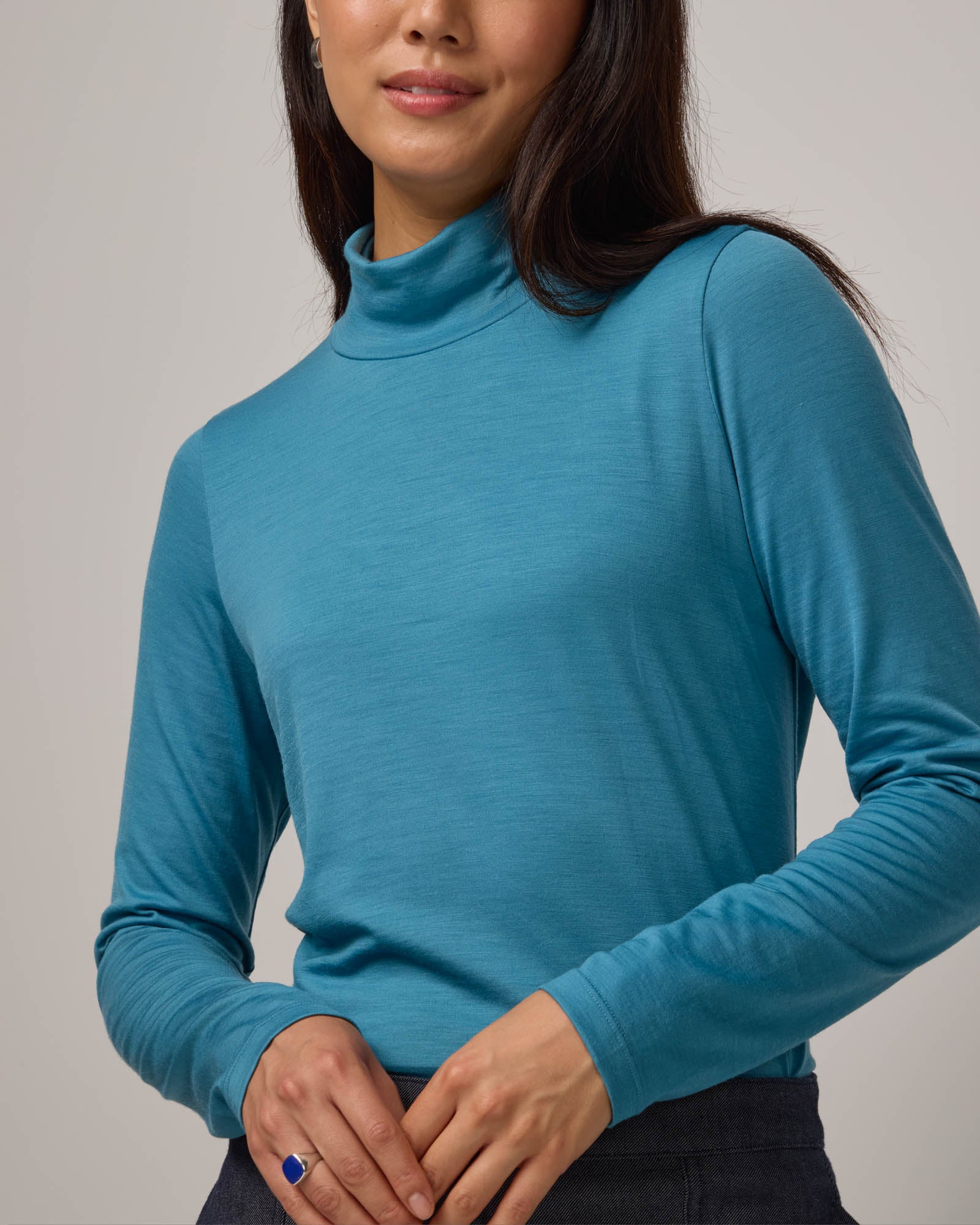 Model wearing Addison Turtleneck Top in Alpine Blue, a glacier ice blue color. Addison Turtleneck Top is a merino wool long sleeve, turtleneck, slim fit top available in sizes XS-3X.