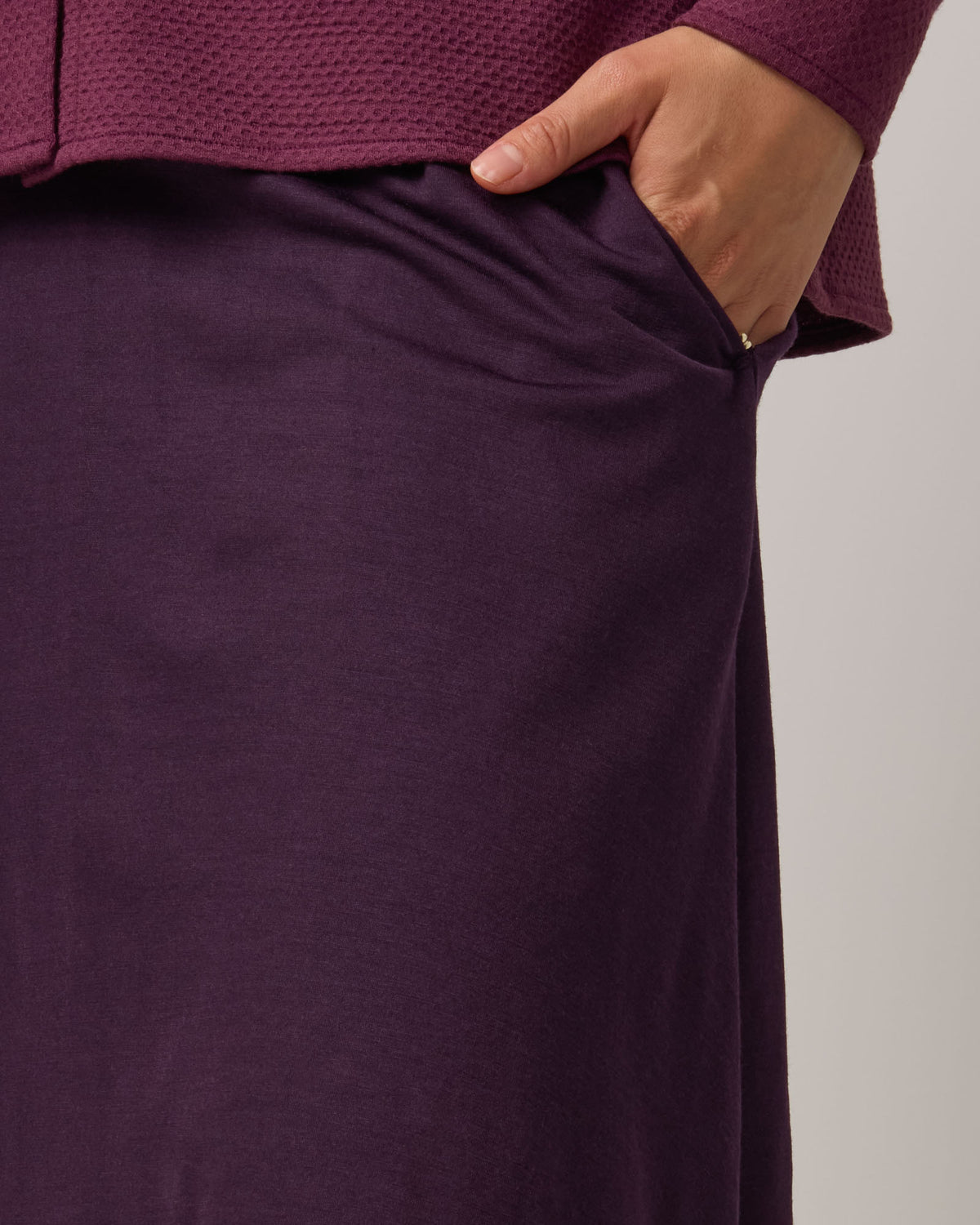 Model wearing Helena Skirt in Cassis, a deep purple color. Helena Skirt is a merino wool knee length skirt with pockets available in sizes XS-3X.