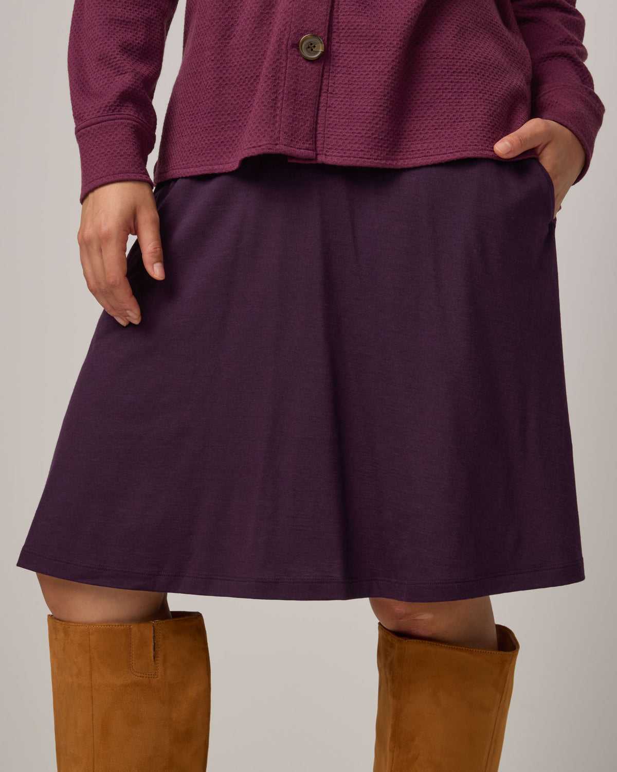 Model wearing Helena Skirt in Cassis, a deep purple color. Helena Skirt is a merino wool knee length skirt with pockets available in sizes XS-3X.