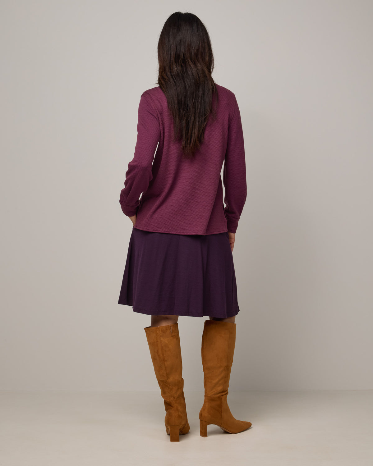 Model wearing Helena Skirt in Cassis, a deep purple color. Helena Skirt is a merino wool knee length skirt with pockets available in sizes XS-3X.