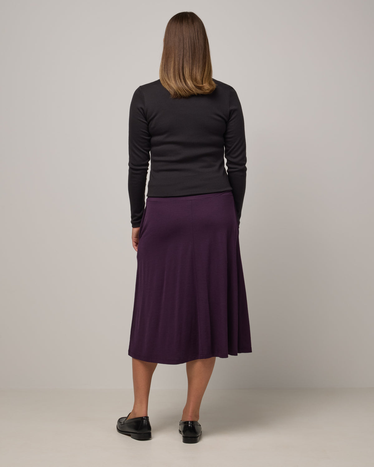Model wearing Helena Midi Skirt in Cassis, a deep purple color. Helena Midi Skirt is a merino wool midi skirt with pockets available in sizes XS-3X.