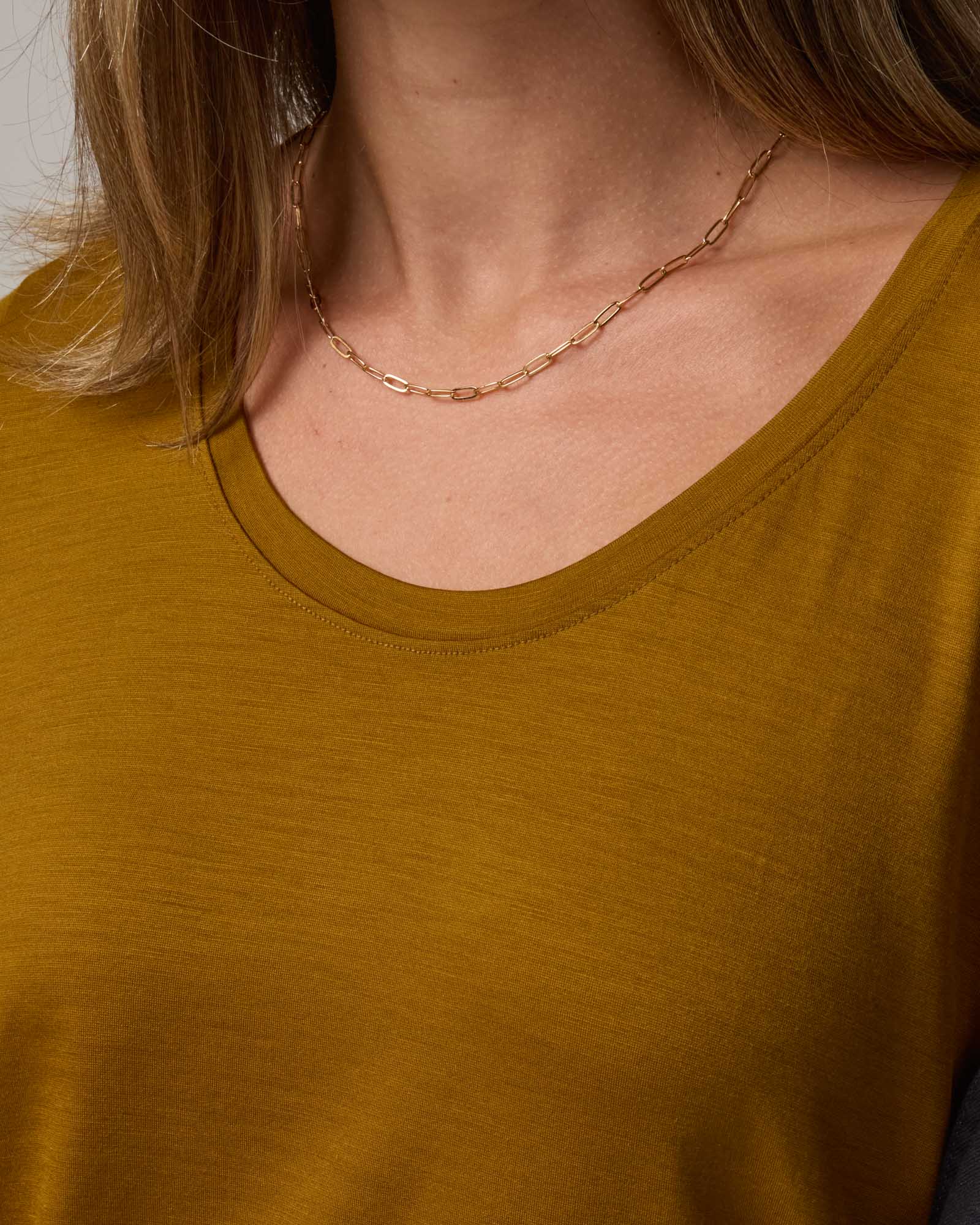 Model wearing Stella Scoop Neck Tee in Spiced Pear, a dark mustard color. Stella Scoop Neck Tee is a merino wool short sleeve, scoop neck t-shirt available in sizes XS-3X.