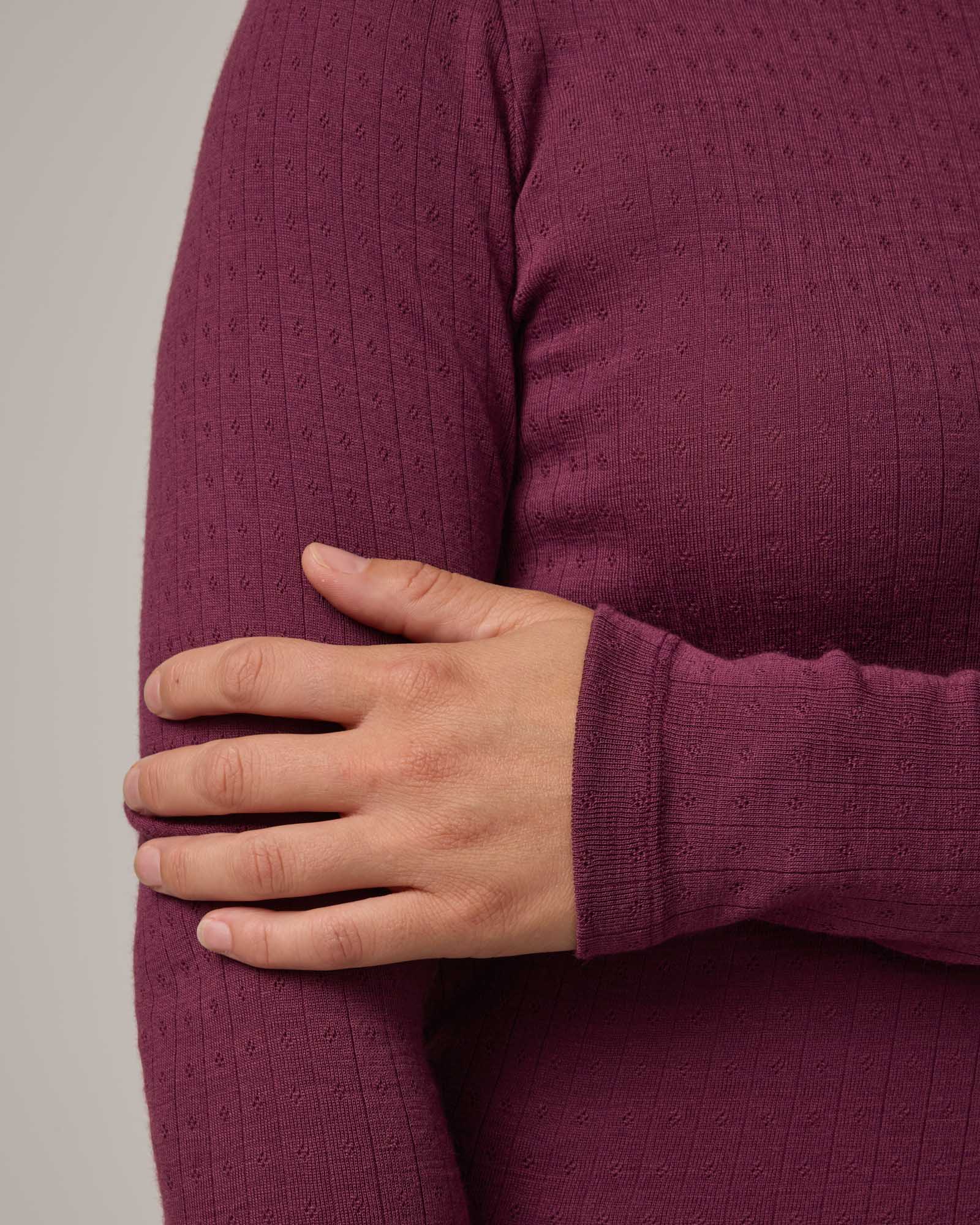 Model wearing Sloan Pointelle Fitted Tee in Plum, a reddish purple color. Sloan Pointelle Fitted Tee is a merino wool long sleeve, crew neck, slim fit tee available in sizes XS-3X.