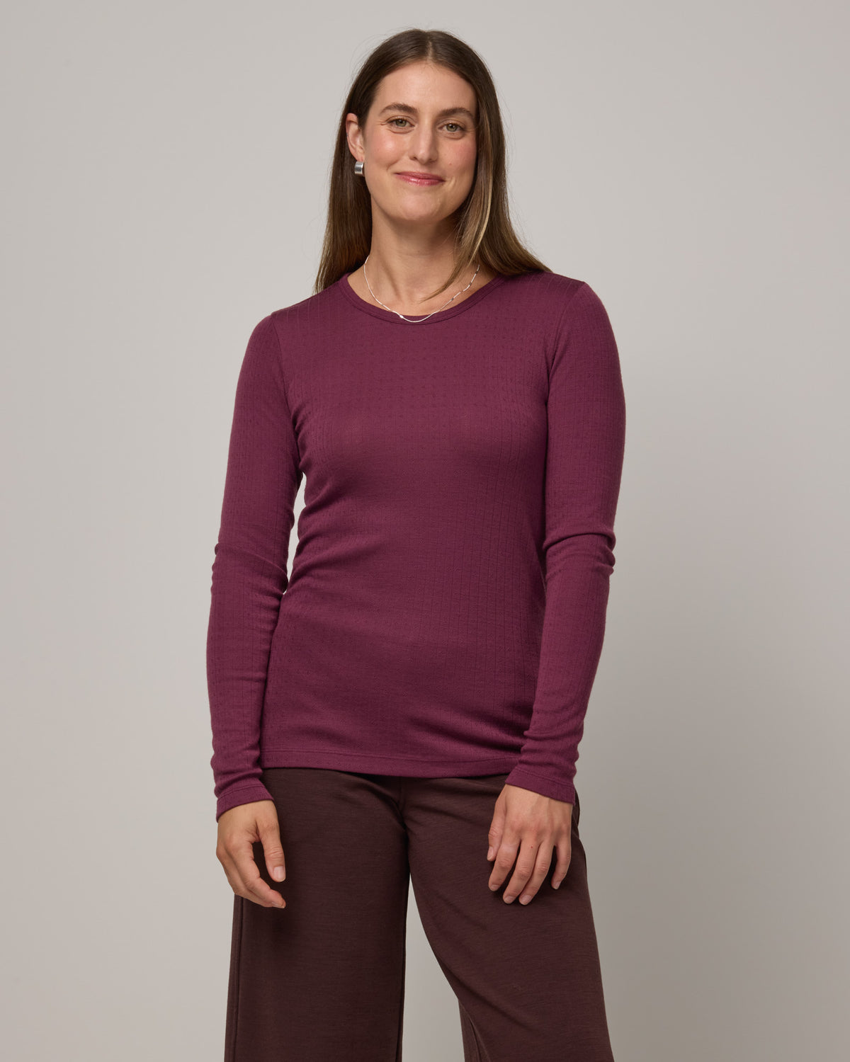 Model wearing Sloan Pointelle Fitted Tee in Plum, a reddish purple color. Sloan Pointelle Fitted Tee is a merino wool long sleeve, crew neck, slim fit tee available in sizes XS-3X.