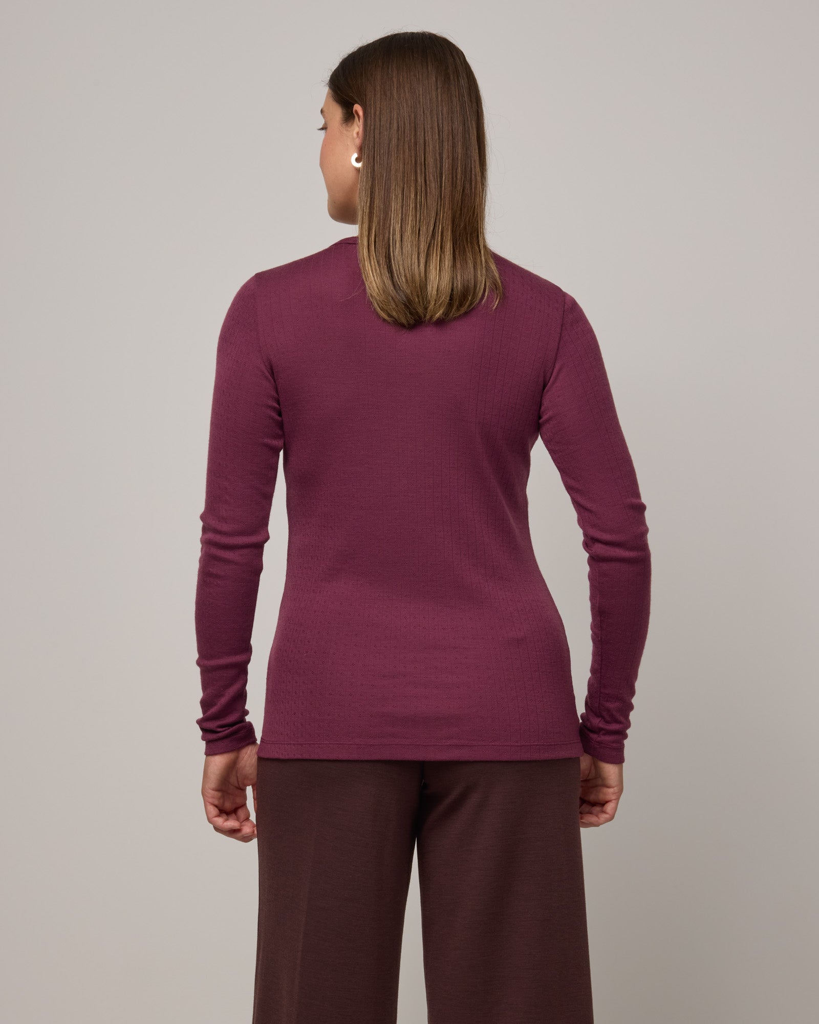 Model wearing Sloan Pointelle Fitted Tee in Plum, a reddish purple color. Sloan Pointelle Fitted Tee is a merino wool long sleeve, crew neck, slim fit tee available in sizes XS-3X.