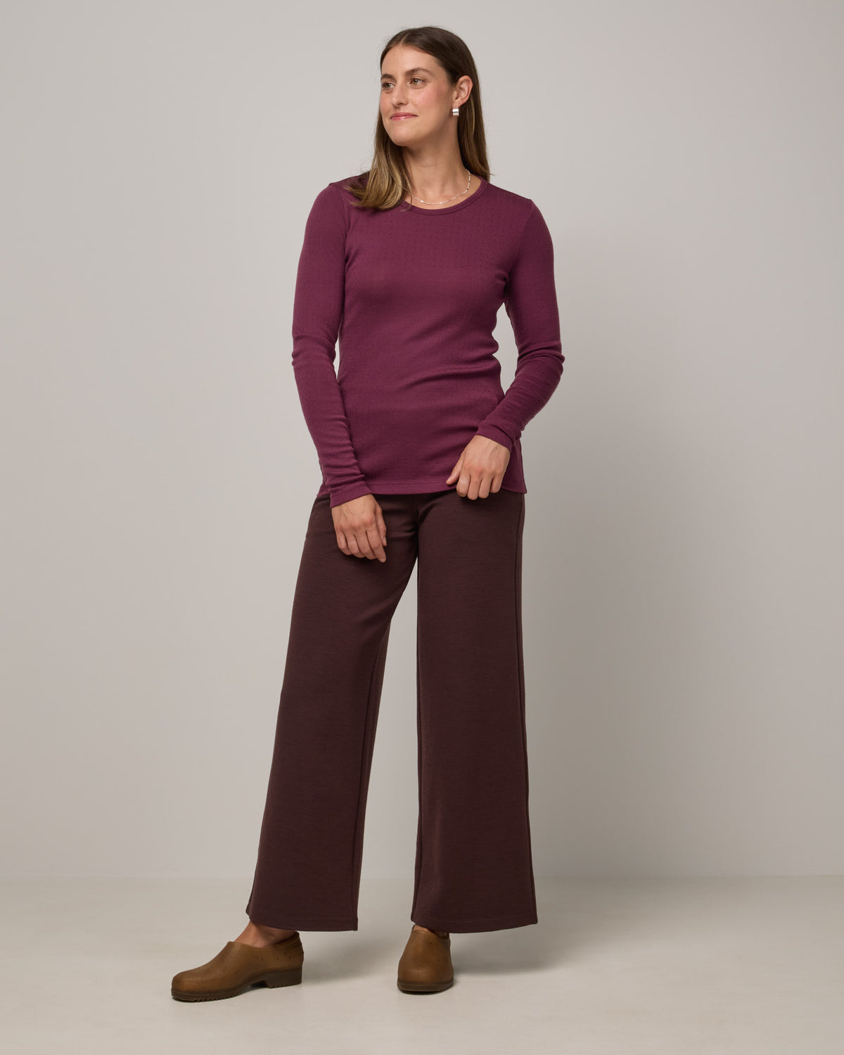 Model wearing Sloan Pointelle Fitted Tee in Plum, a reddish purple color. Sloan Pointelle Fitted Tee is a merino wool long sleeve, crew neck, slim fit tee available in sizes XS-3X.
