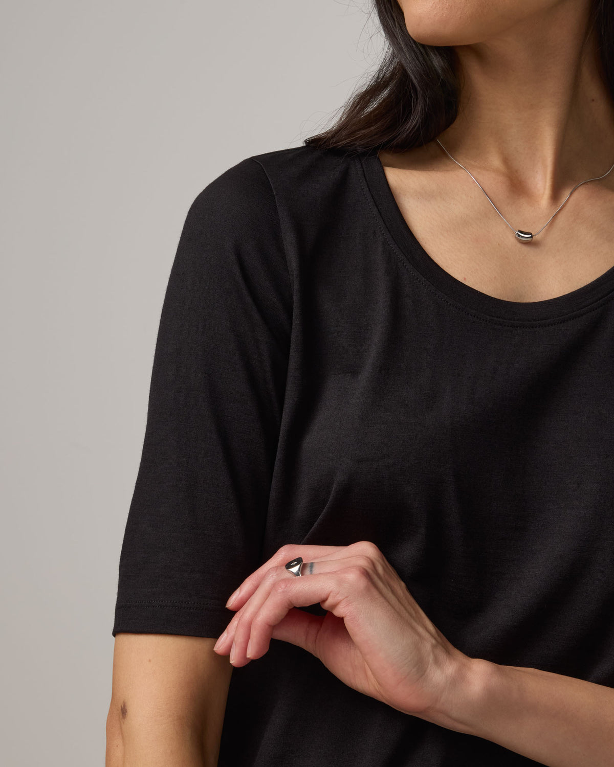 Model wearing Celine Signature Elbow Sleeve Tee in Black. Celine Signature Elbow Sleeve Tee is a merino wool scoop neck tee available in sizes XS-3X.
