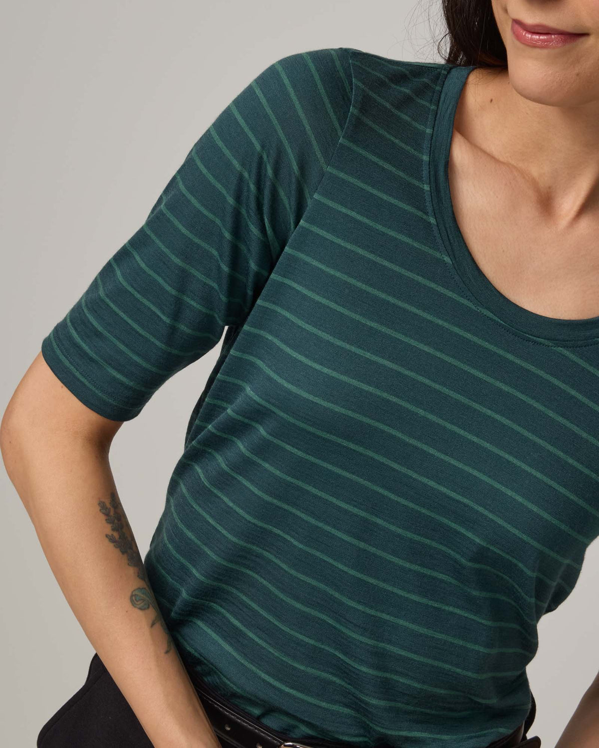 Model wearing Celine Signature Elbow-Sleeve Tee in Pine & Emerald Stripe, a dark green stripe. Celine Signature Elbow Sleeve Tee is a merino wool scoop neck half-sleeve tee available in sizes XS-3X.