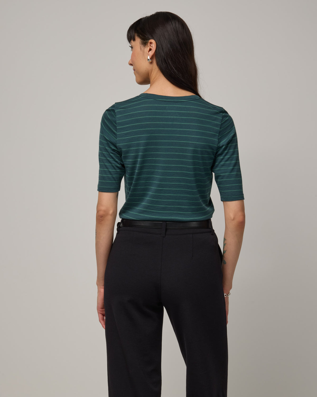 Model wearing Celine Signature Elbow-Sleeve Tee in Pine & Emerald Stripe, a dark green stripe. Celine Signature Elbow Sleeve Tee is a merino wool scoop neck half-sleeve tee available in sizes XS-3X.