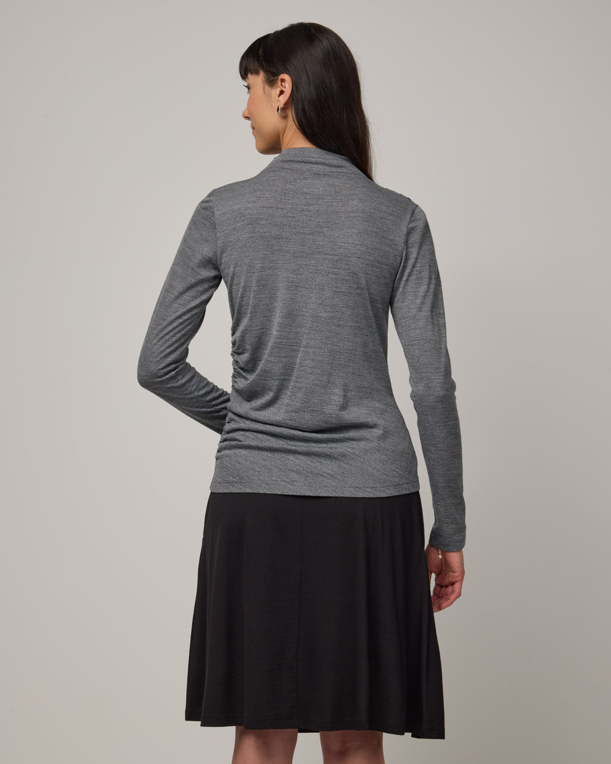 Model wearing Katrina Ruched Top in Charcoal Heather, a heathered dark gray color. Katrina Ruched Top is a long sleeve fitted merino wool mock-turtleneck top available in sizes XS-XXL.