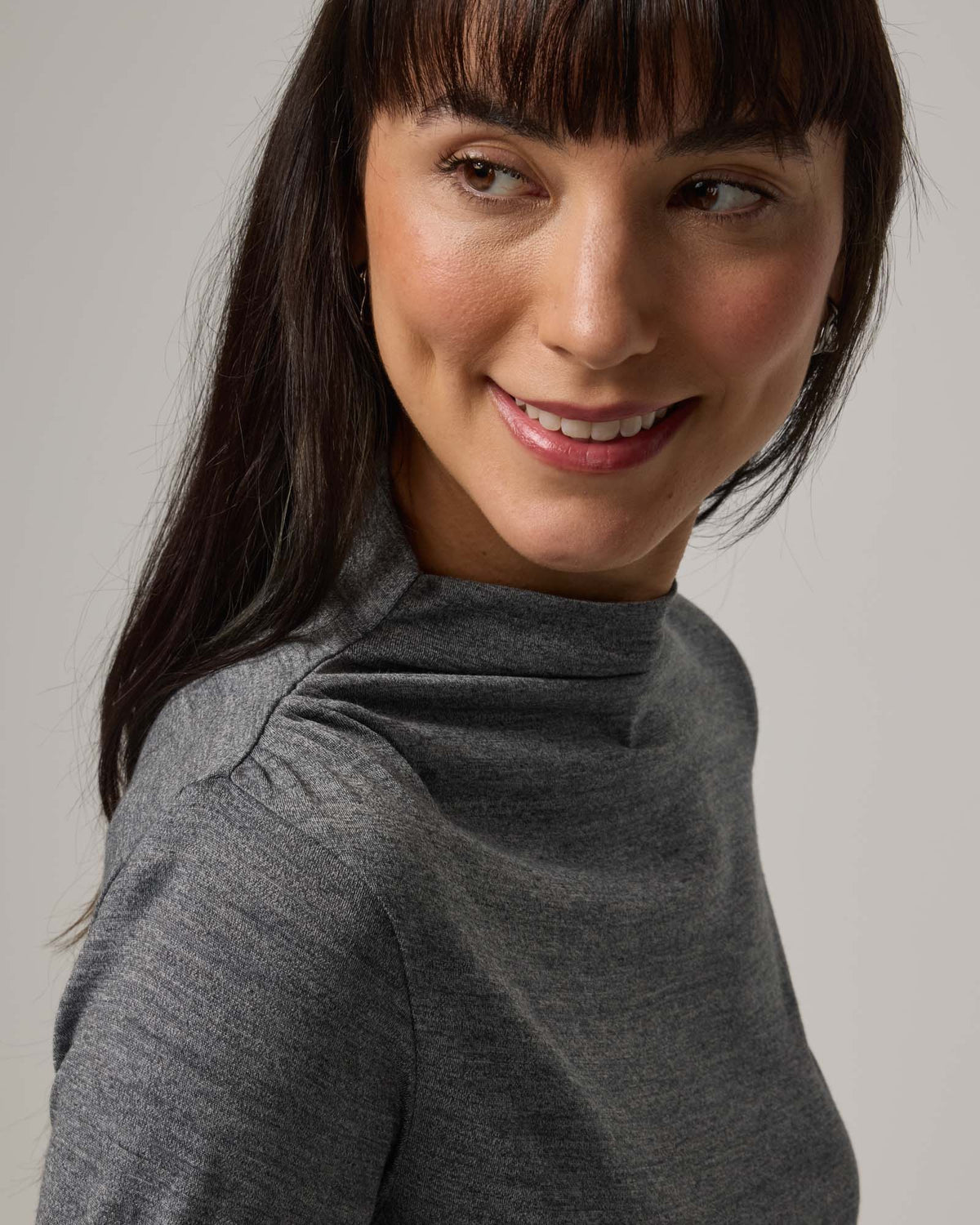 Model wearing Katrina Ruched Top in Charcoal Heather, a heathered dark gray color. Katrina Ruched Top is a long sleeve fitted merino wool mock-turtleneck top available in sizes XS-XXL.
